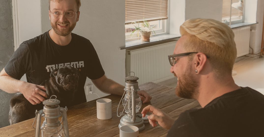Two happy employees from The Bearded Ladies enjoying a cup of coffee together. One of them has a dog in his lap.