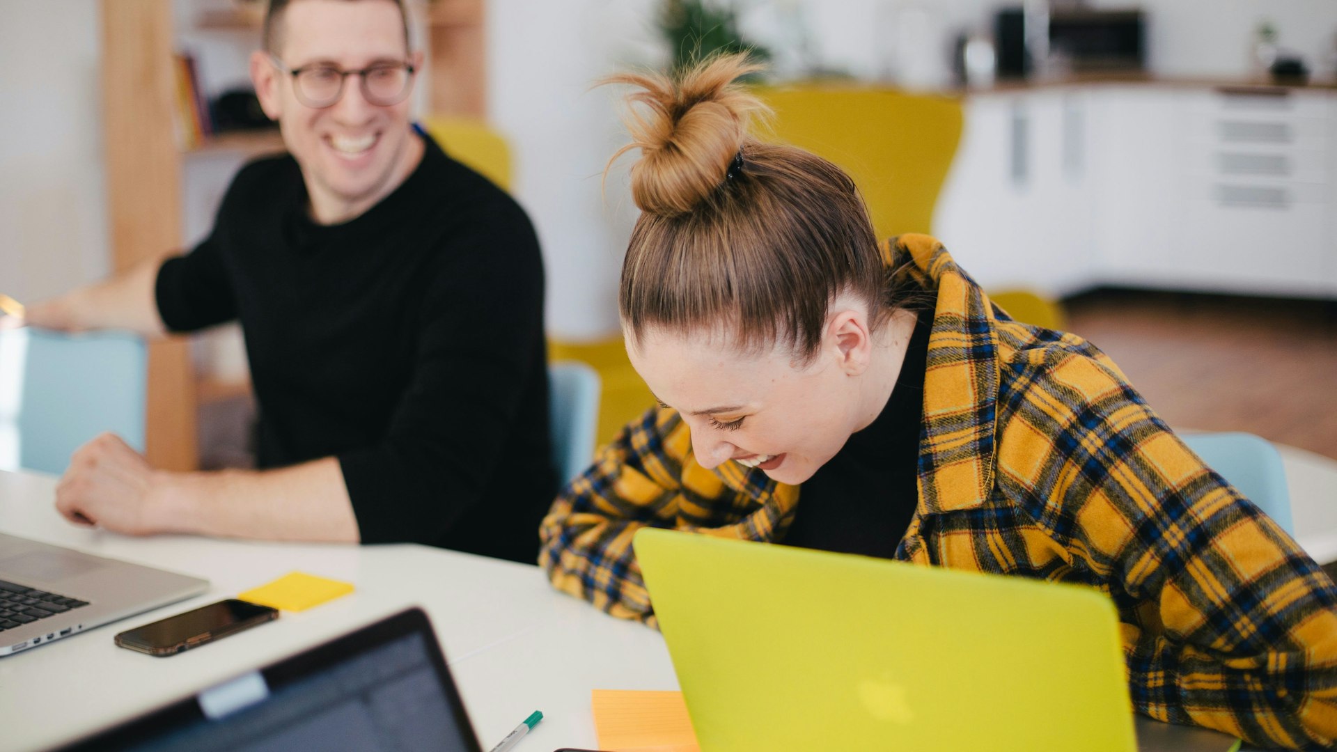 A man and a woman in an office environment. Both of them are laughing.