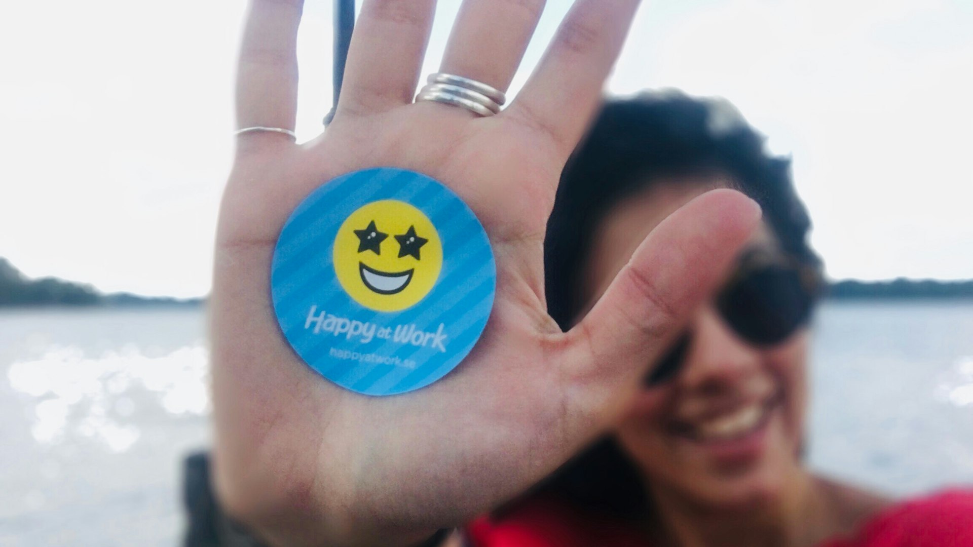 Ett klistermärke med Happy at Works logotyp fastklistrad på en handflata.