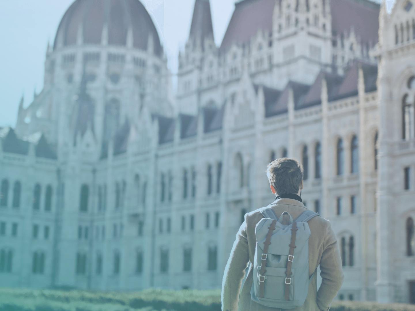 A man with a backpack is standing in front of the Hungarian parliament building.