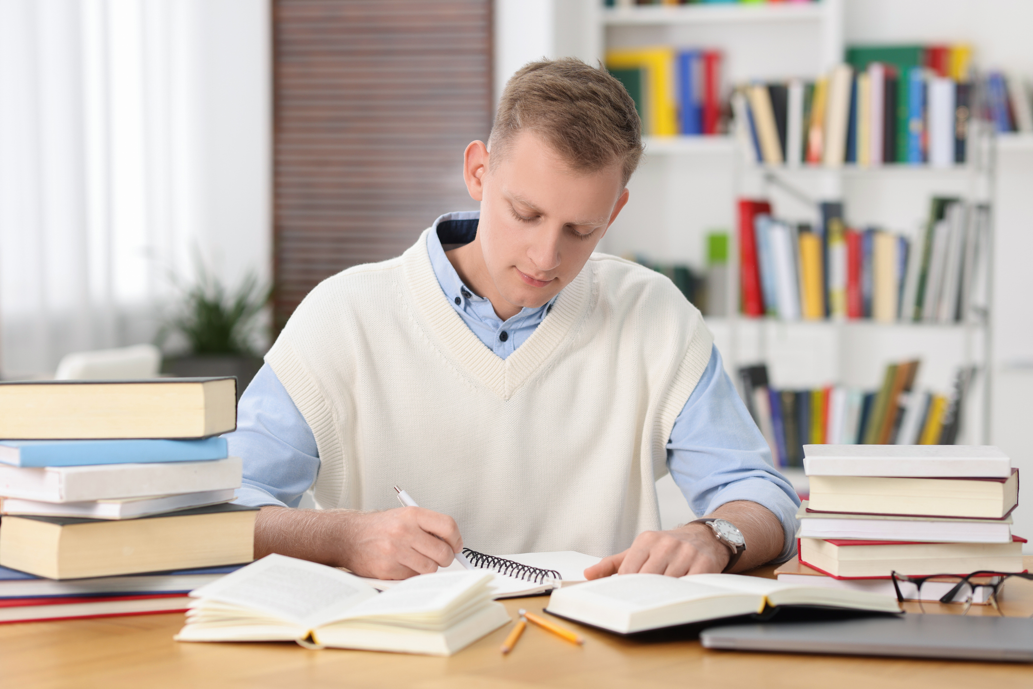 Male student studying with stacks of books surrounding him on his desk