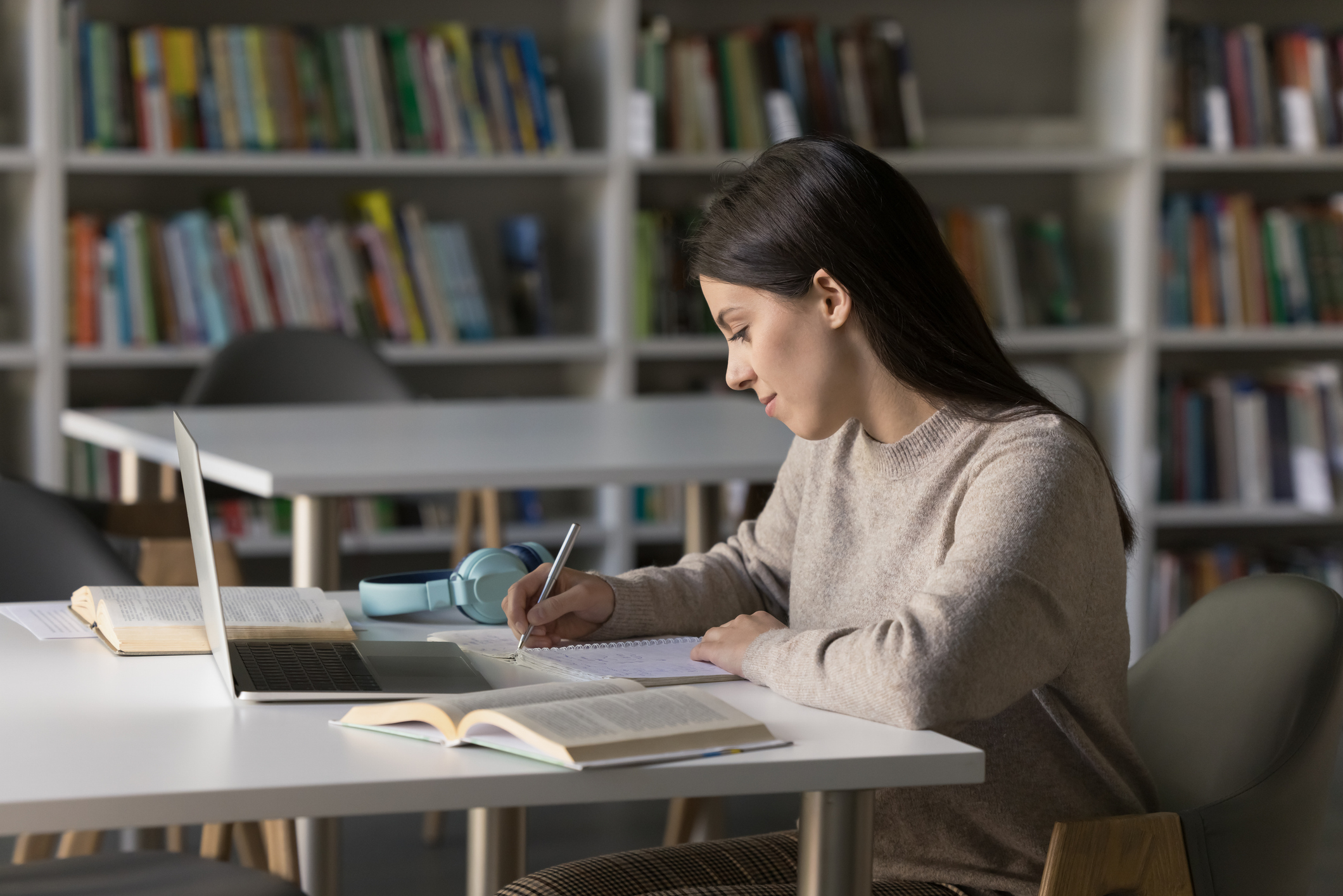 Female student with her laptop open writing something down in her notebook