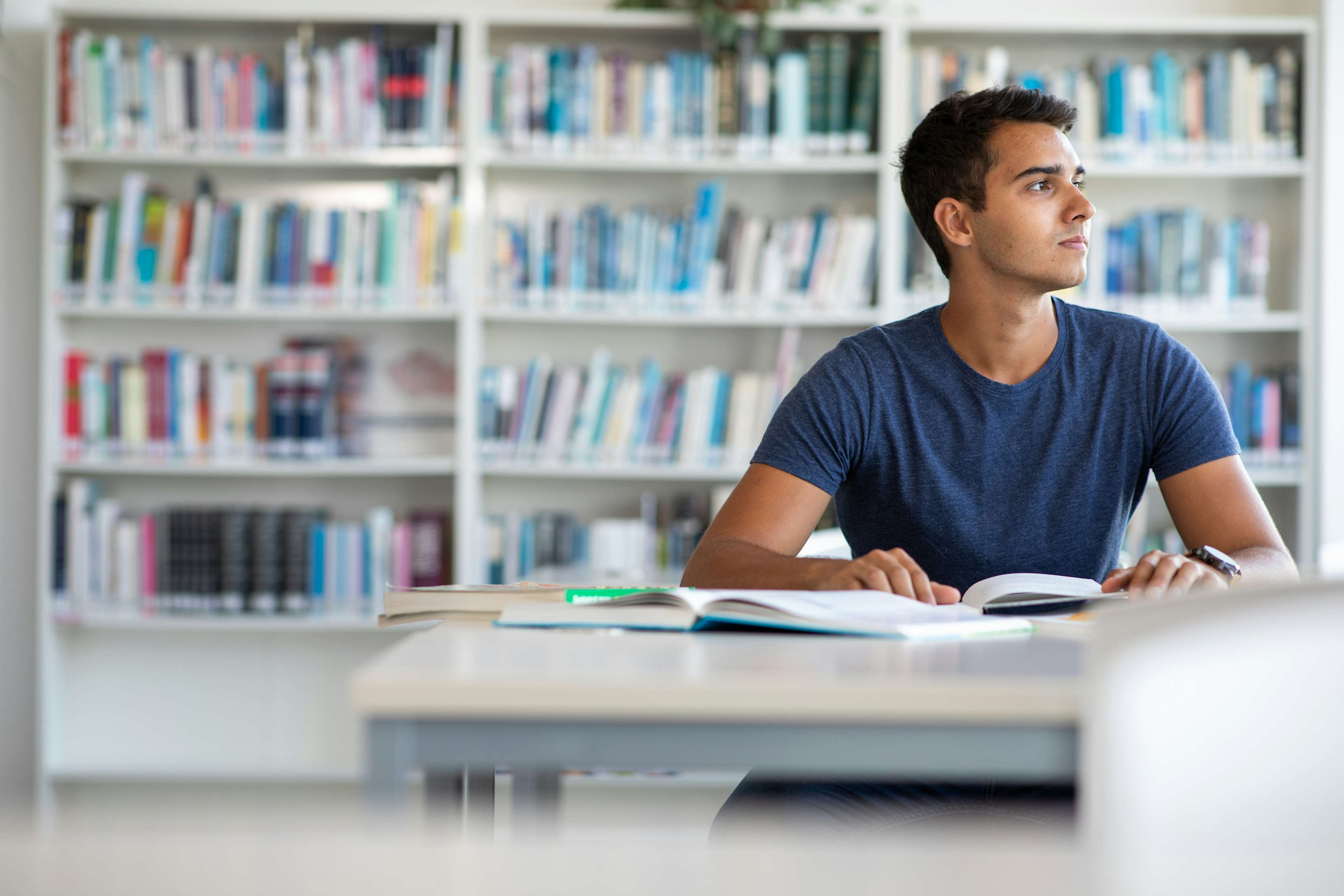 Male student sitting in a library taking a break from studying