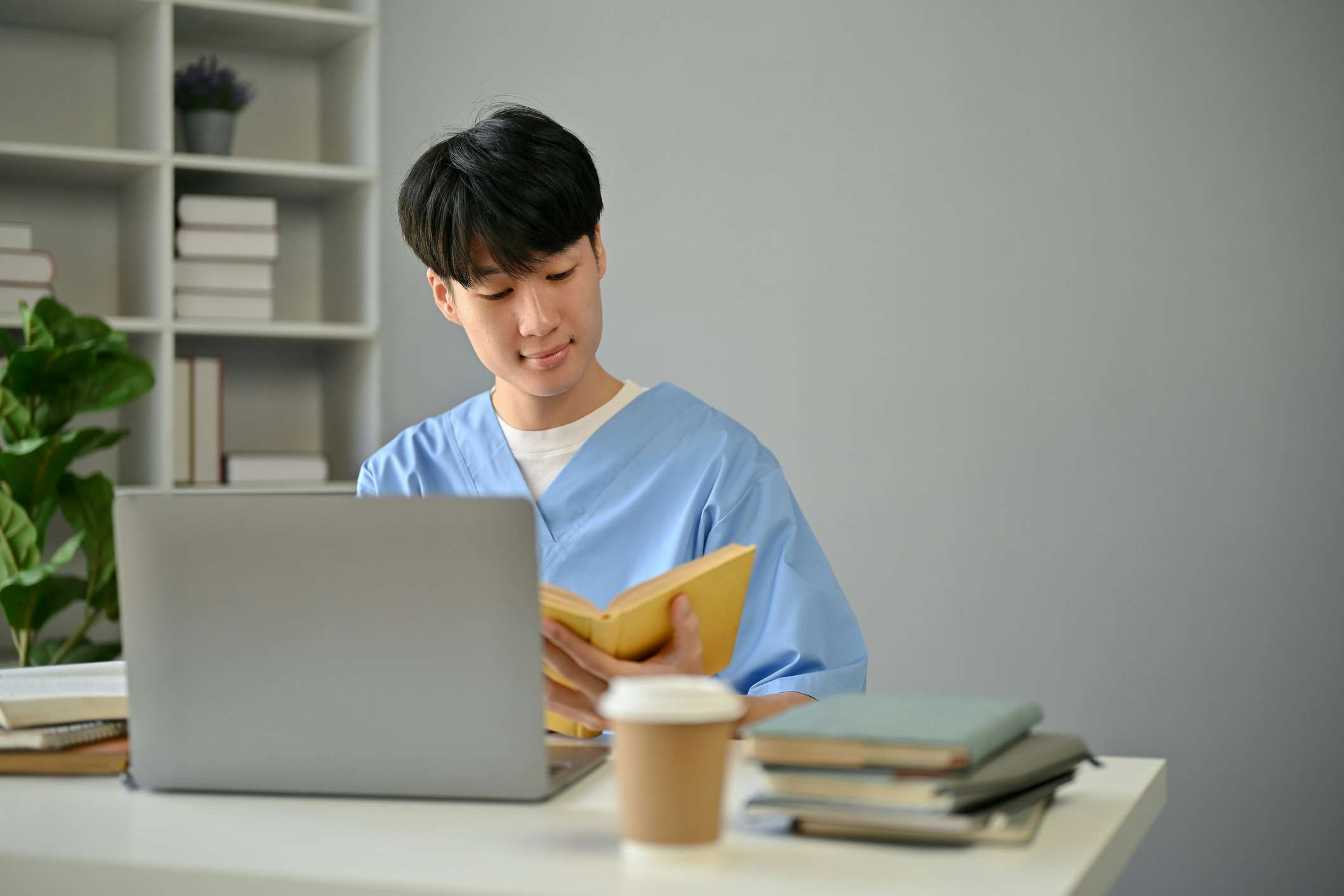 Male student sitting in front of his laptop reading a book