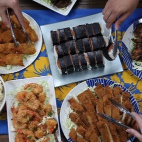 Buffet line with fried shrimp, garlic shrimp, chicken katsu, and musubi.