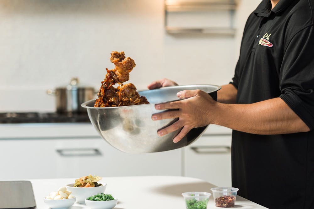 chef mixing fried chicken with sauce