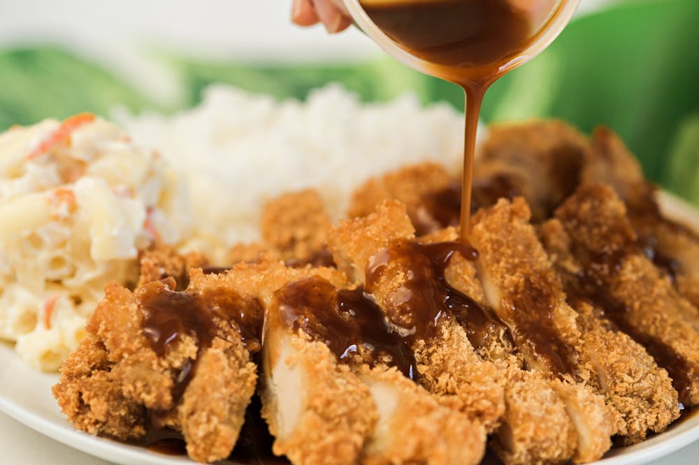 L&L Chicken Katsu with plate with Katsu sauce being poured over the katsu.