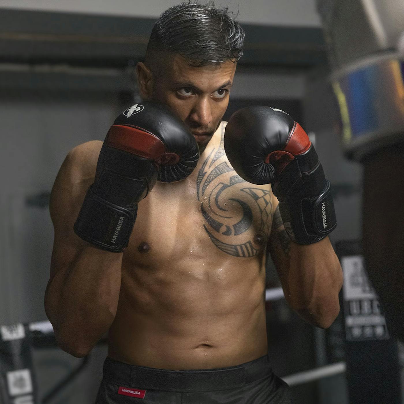 A male boxer in a gym wearing black/red Hayabusa T3 Boxing Gloves squared up and focused on his sparring partner.