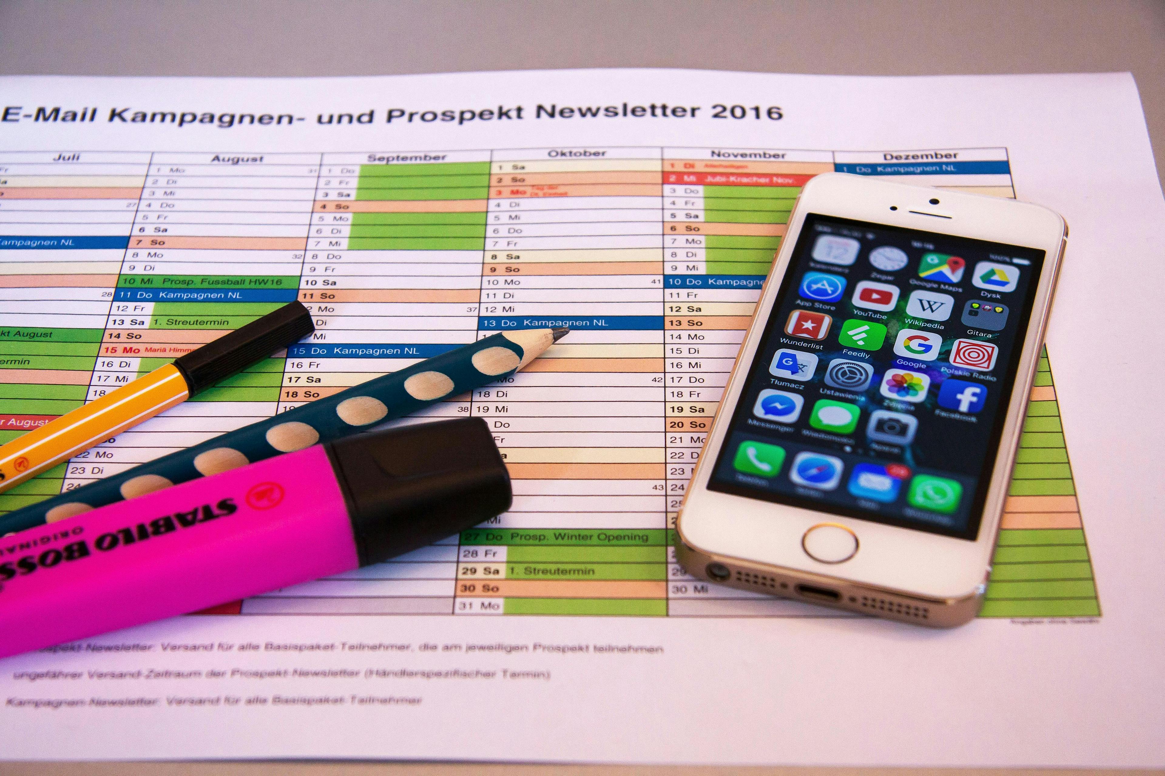 picture of a calendar with a felt tip liner, a pencil and a highlighter laying on the left side and an iphone laying on the right side