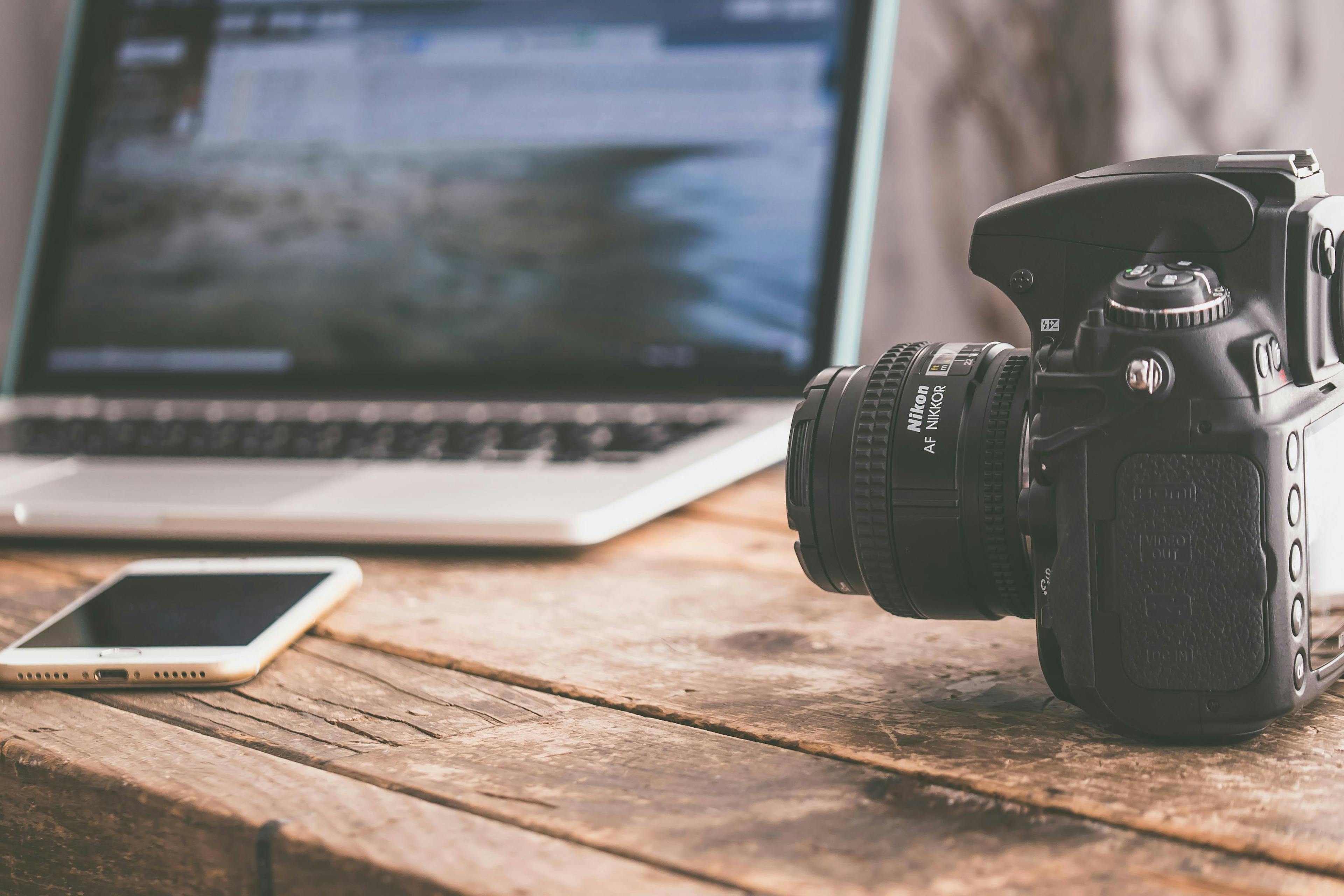 A Laptop, Iphone and Nikon Camera on a desk