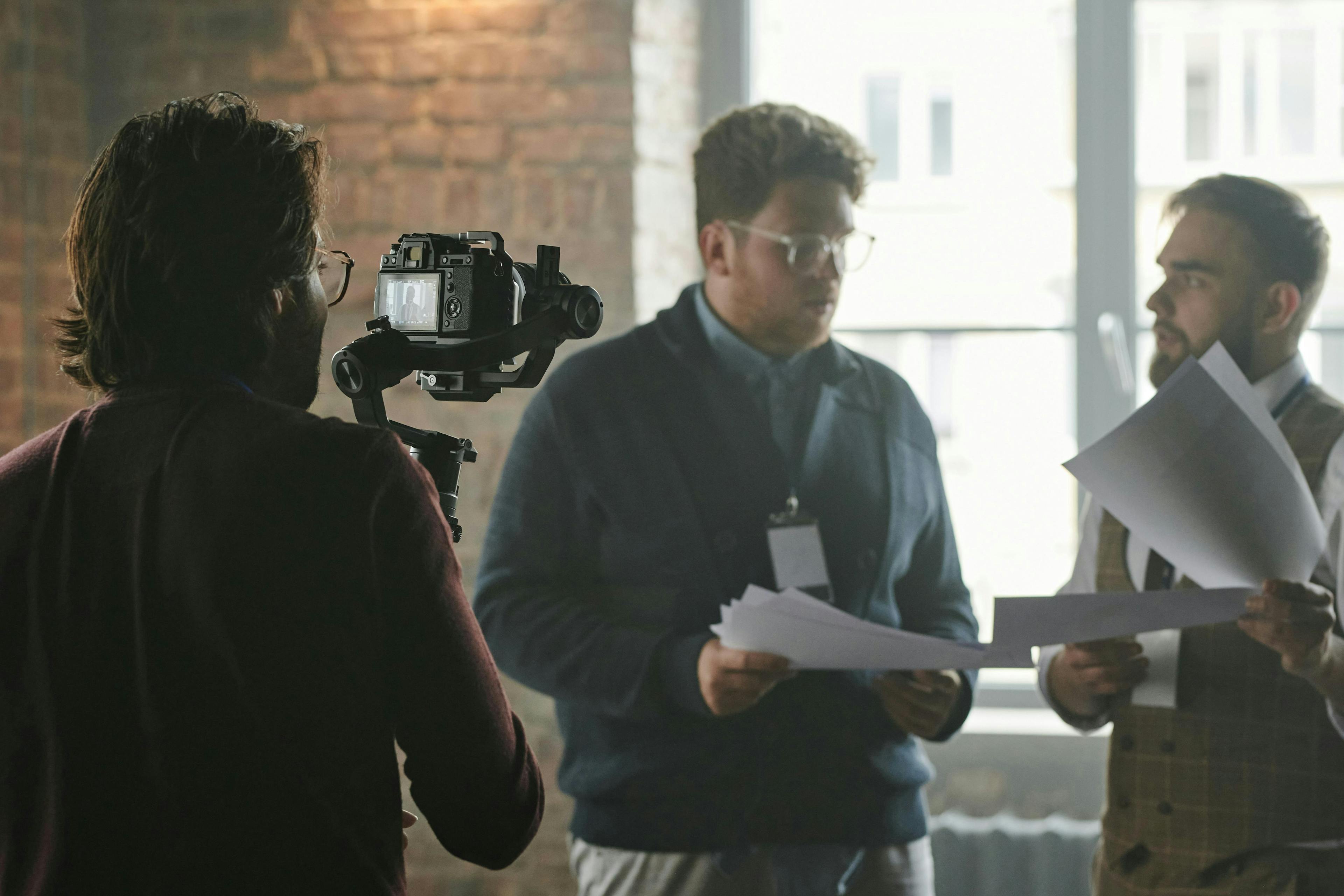 Videoshoot with two men facing each other and holding various papers. we can see the camera man from the back holding the videocamera on a gimble