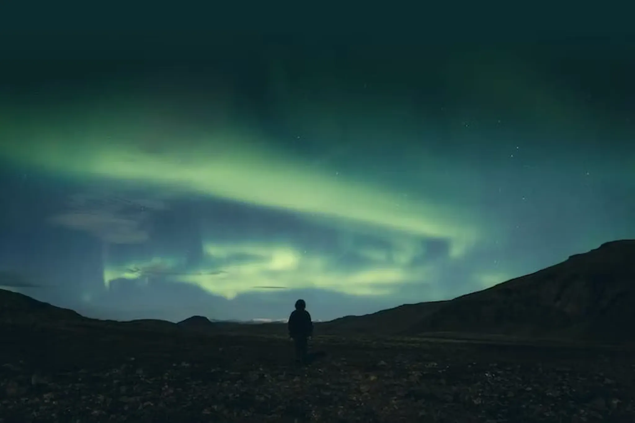 A person watching the Northern Lights over a mountain