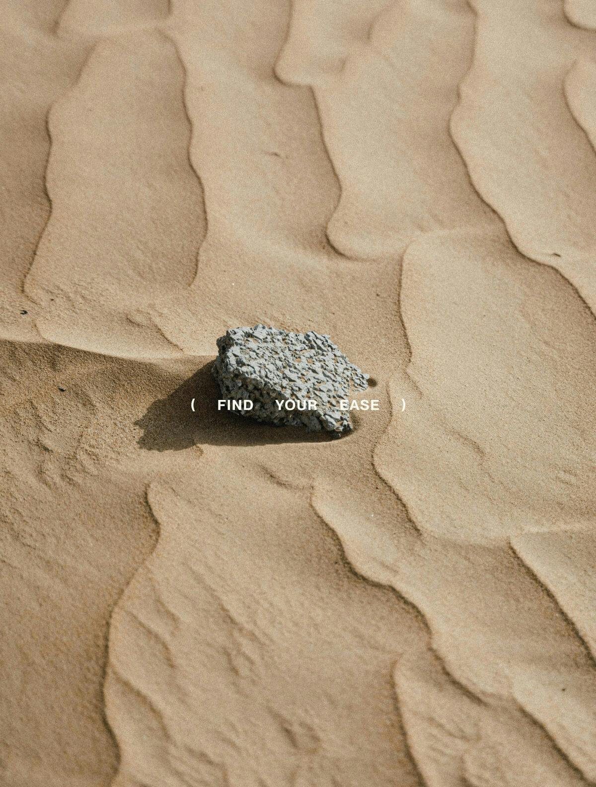 rock laying in sand with FIND YOUR EASE overlayed on top of image