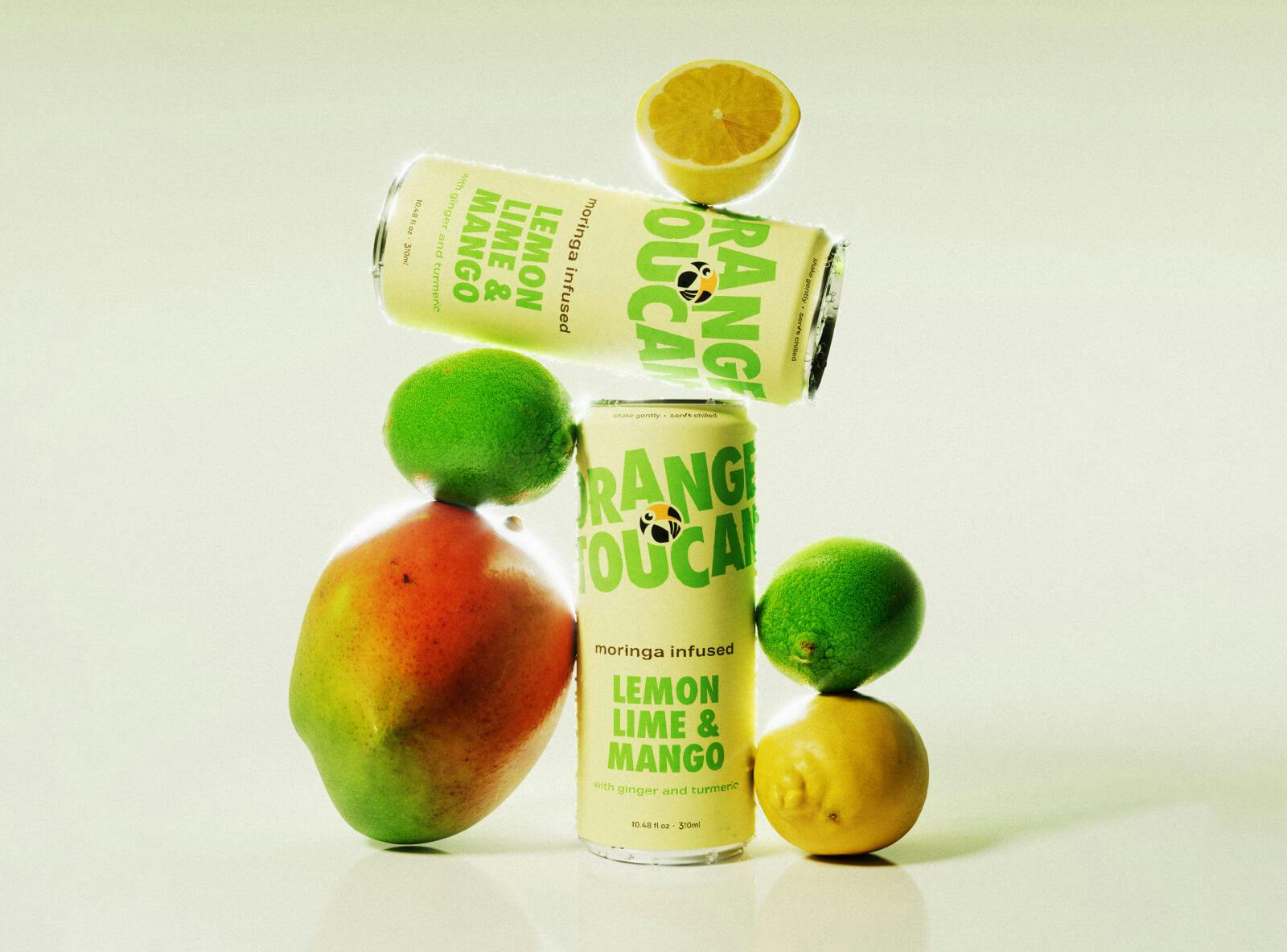 Two aluminum cans of Orange Toucan beverage stacked on fruit