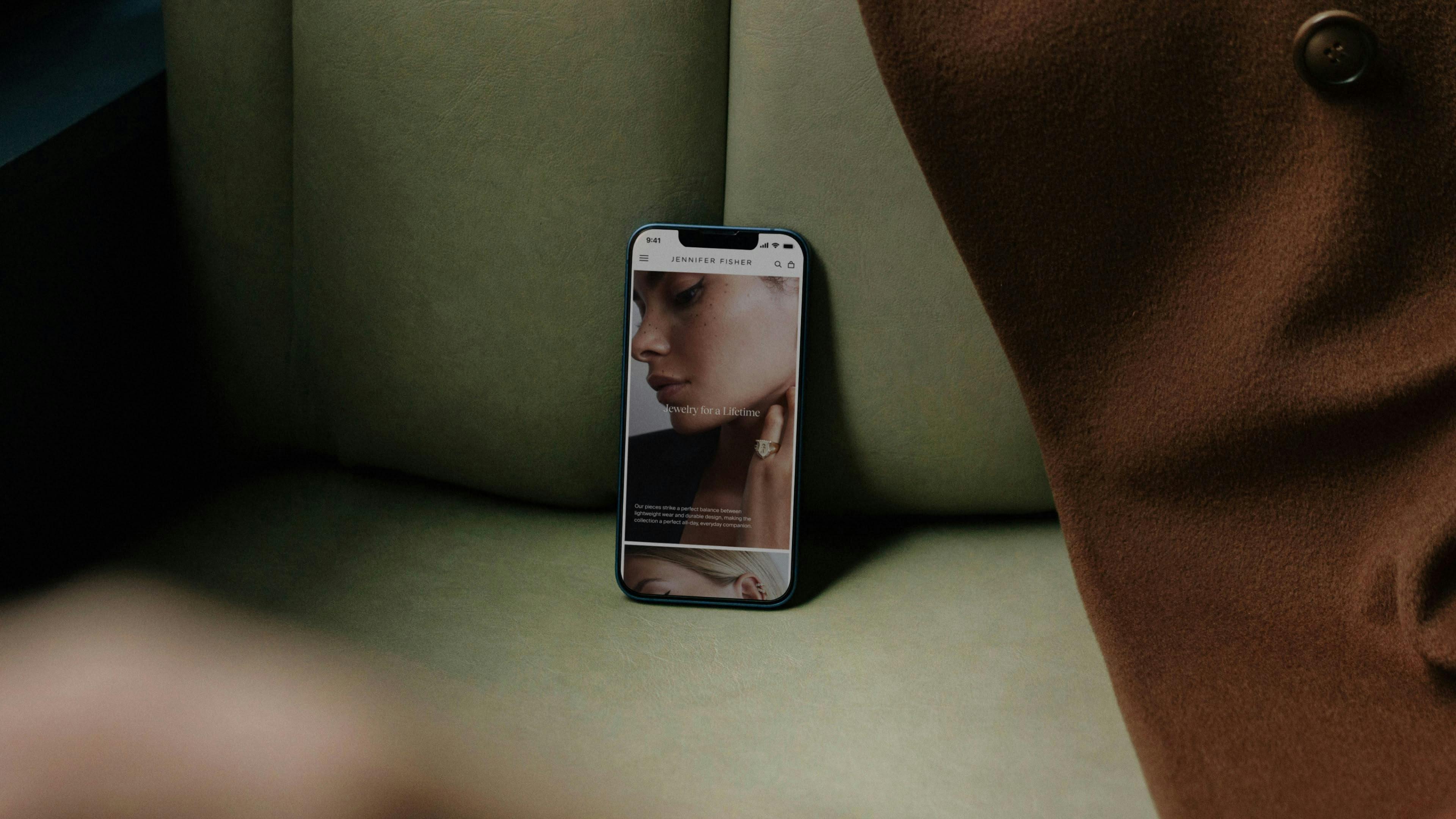 iphone on couch with screenshot of JENNIFER FISHER website