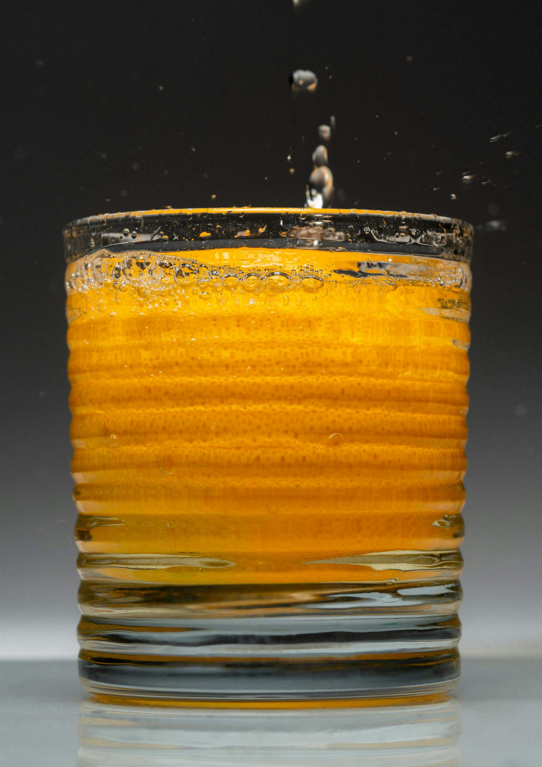 A glass with a full orange inside with liquid pouring on top