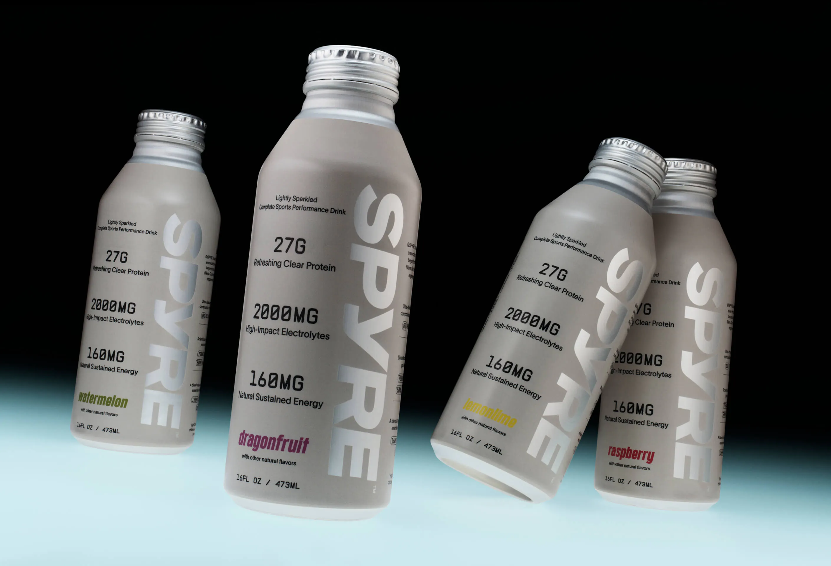 Four SPYRE performance drink bottles in watermelon, dragonfruit, lemon-lime, and raspberry flavors arranged in a dynamic floating composition against a dark background with teal gradient floor