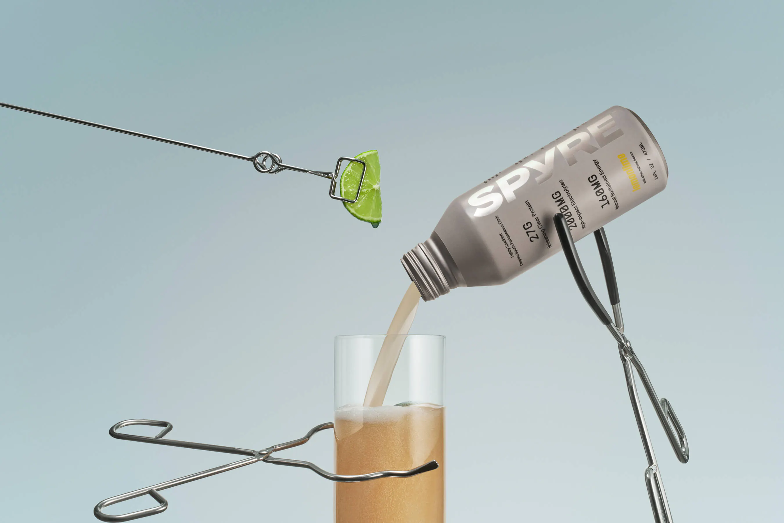 SPYRE lemon-lime performance drink bottle tipped and pouring into a glass, surrounded by floating surgical clamps and a lime wedge held by a wire loop, against a soft teal background
