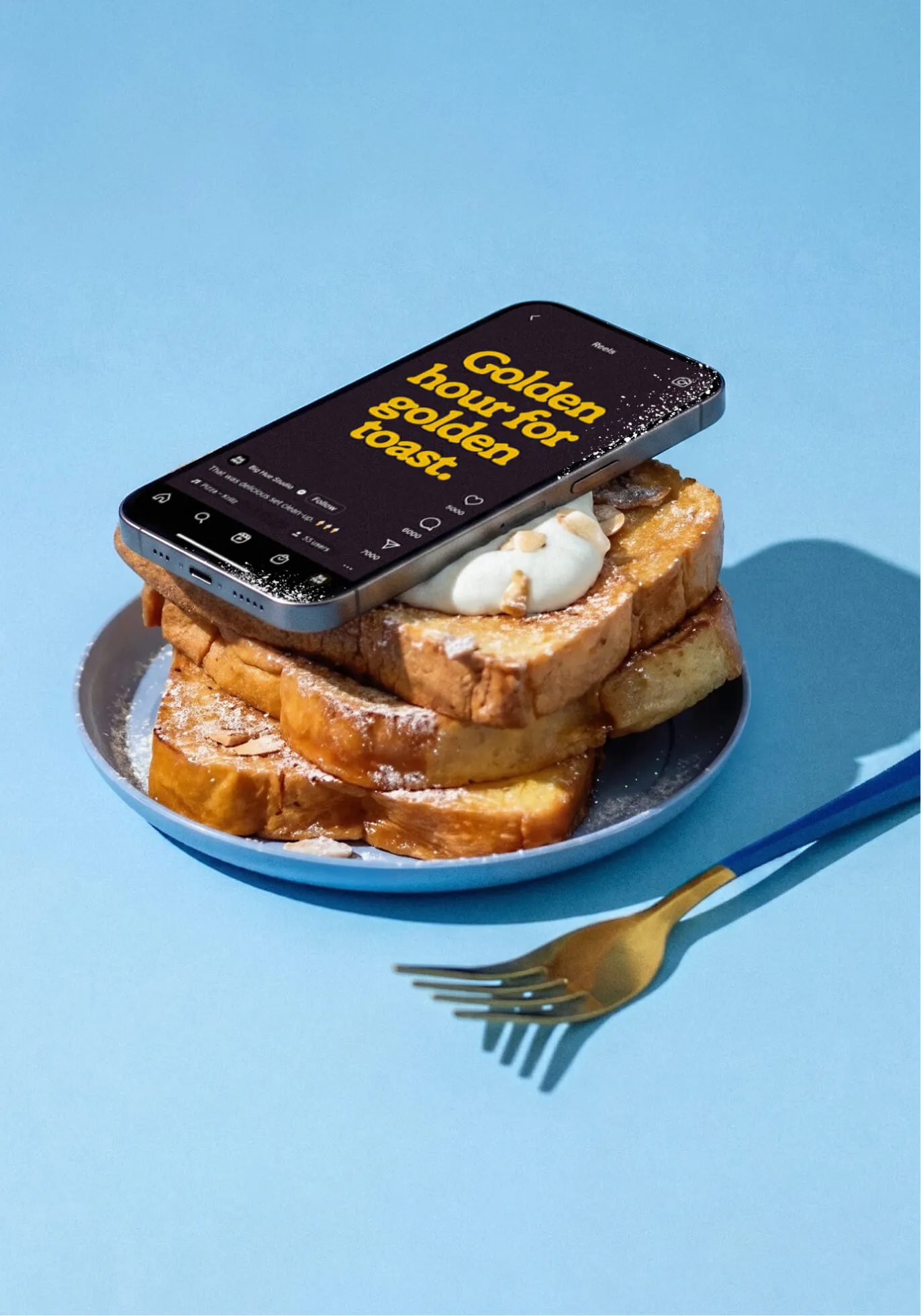 A smartphone propped against a stack of French toast on a blue plate, beside a gold fork on a light blue surface. The phone screen shows an Instagram Reel with the headline "Golden hour for golden toast." in yellow Ramboia Bold on dark background.