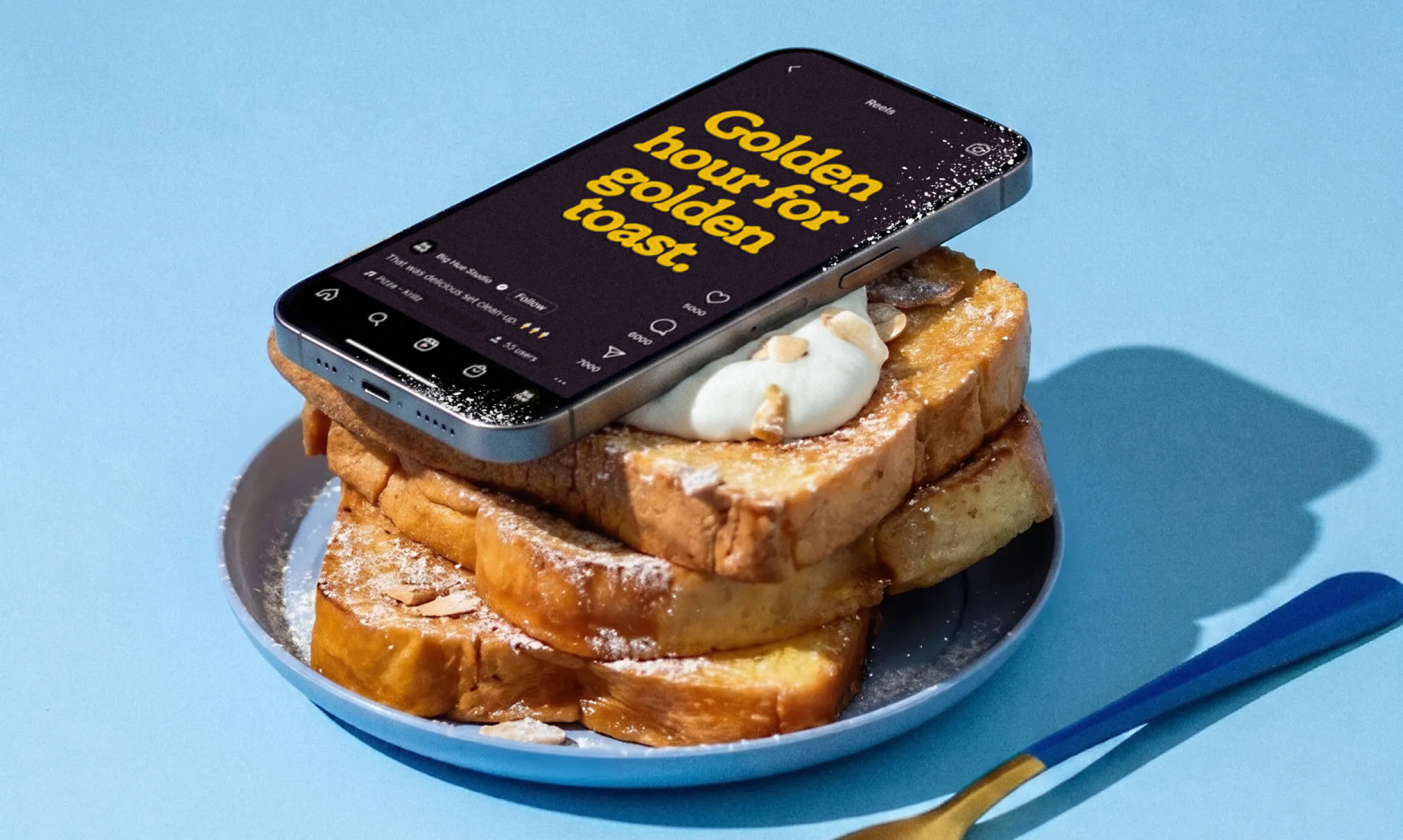 A smartphone propped against a stack of French toast on a blue plate, beside a gold fork on a light blue surface. The phone screen shows an Instagram Reel with the headline "Golden hour for golden toast." in yellow Ramboia Bold on dark background.