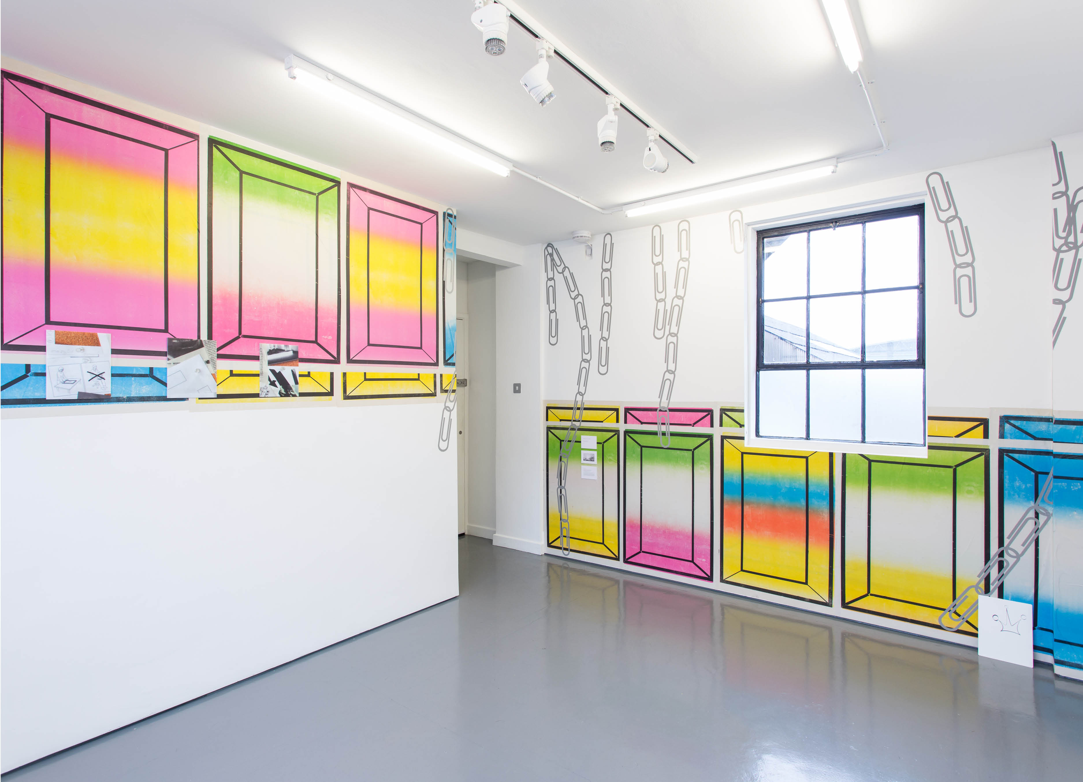 Installation view of 'Half' by henry Coleman, brightly colored posters overlap to horizontally  fill  half the available wall space of a small gallery space with other artworks mounted over the surface