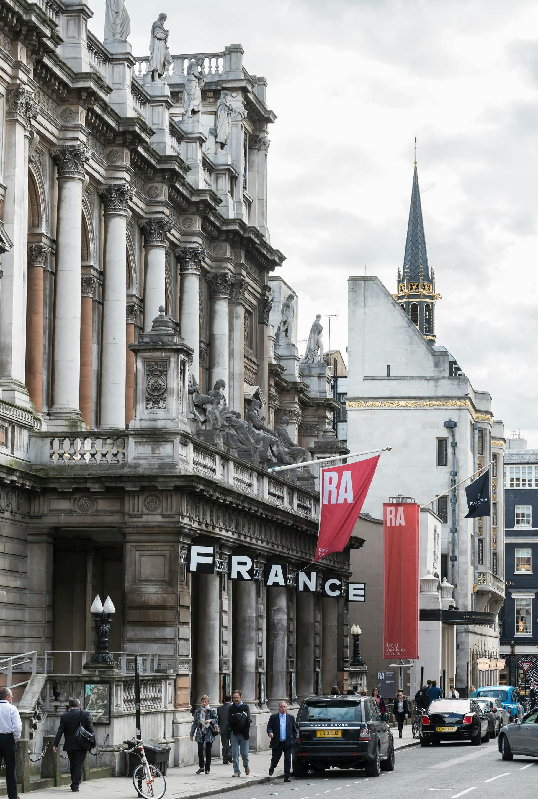 'Scrape' by UK artist Henry Coleman. Architectural installation of illuminated signage spelling out the word FRANCE attached to the facade of the RA building 6 Burlington Gardens, London, with red RA flags and banners in the background