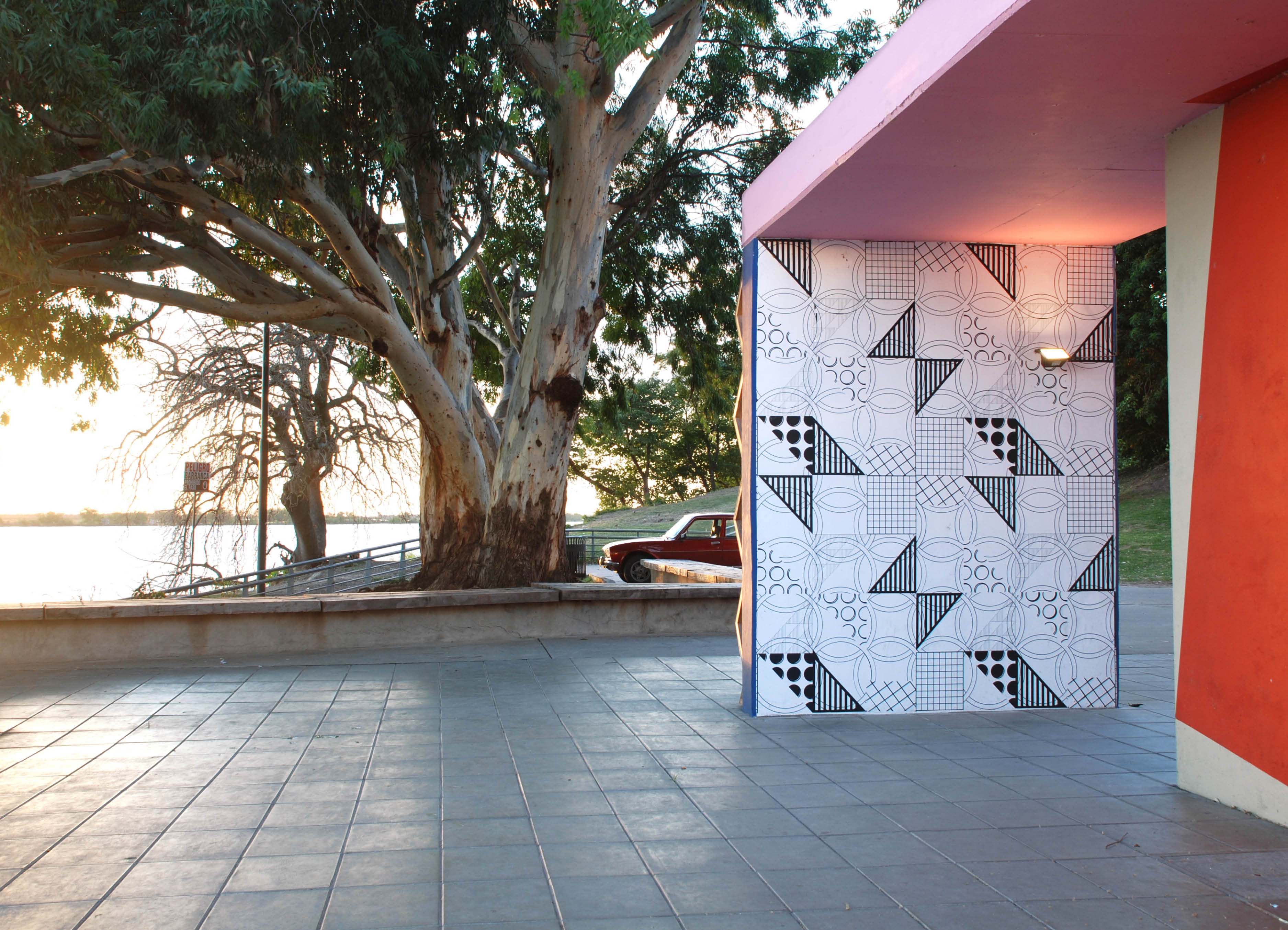 'Telon'  by Henry Coleman and Cristina Schiavi, geometric wall painting and brightly colored murals shown against a morning sky at the MACRO museum, Rosario, with the Paraná river in the background