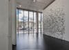 'About now' exhibition by Henry Coleman at Bloomberg SPACE, a large pattern of painted tiles are mounted across a wall in the pattern of a terrazo floor from the nearby Barbican Centre, A voile curtain with decorative elements runs across the windows 