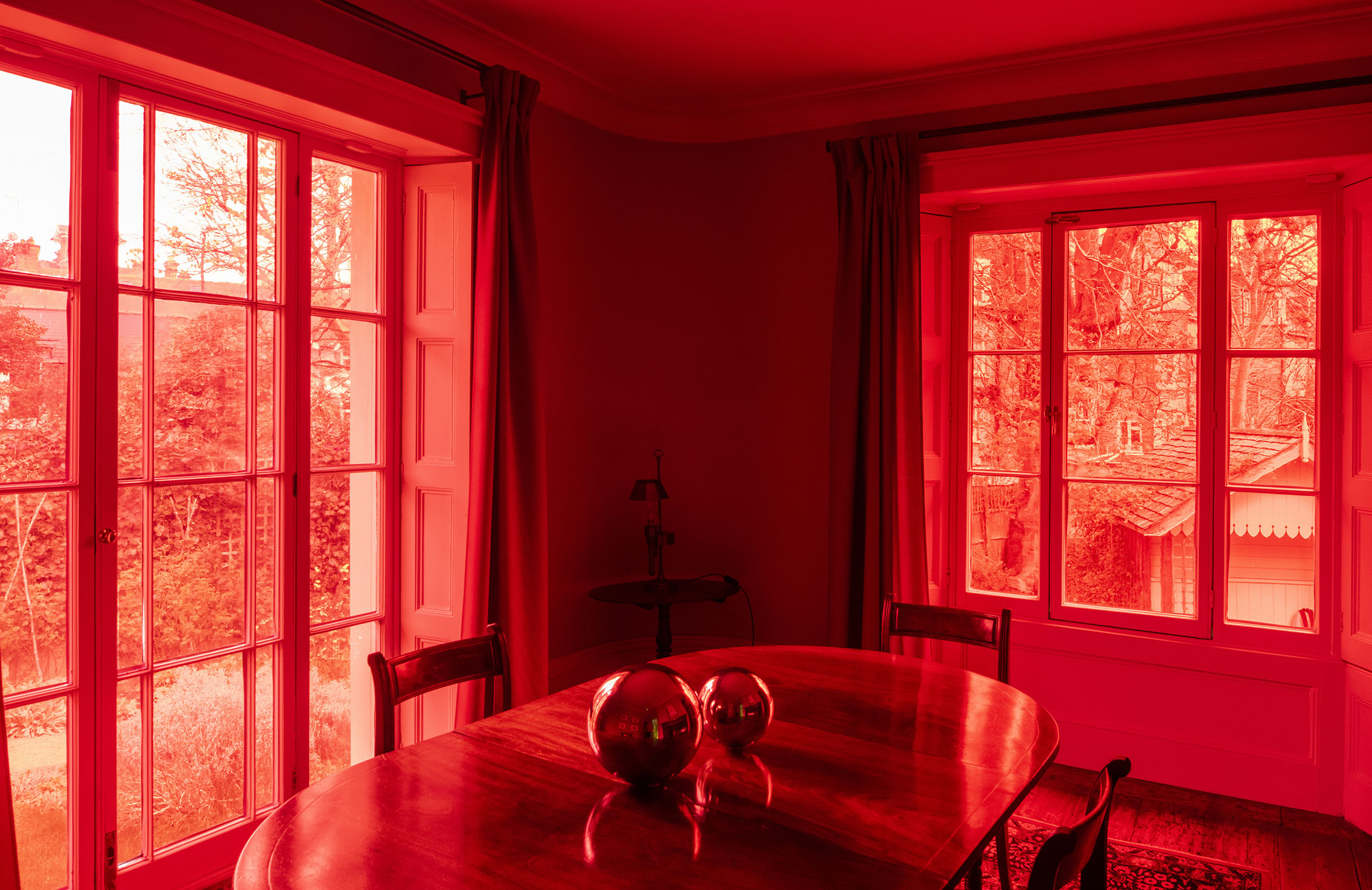 The effects', Sculptural installation by artist Henry Coleman. Dining room of JMW Turner's House, Sandycombe Lodge with red colored light coming through the garden windows, two reflective globes sit on an ornate table