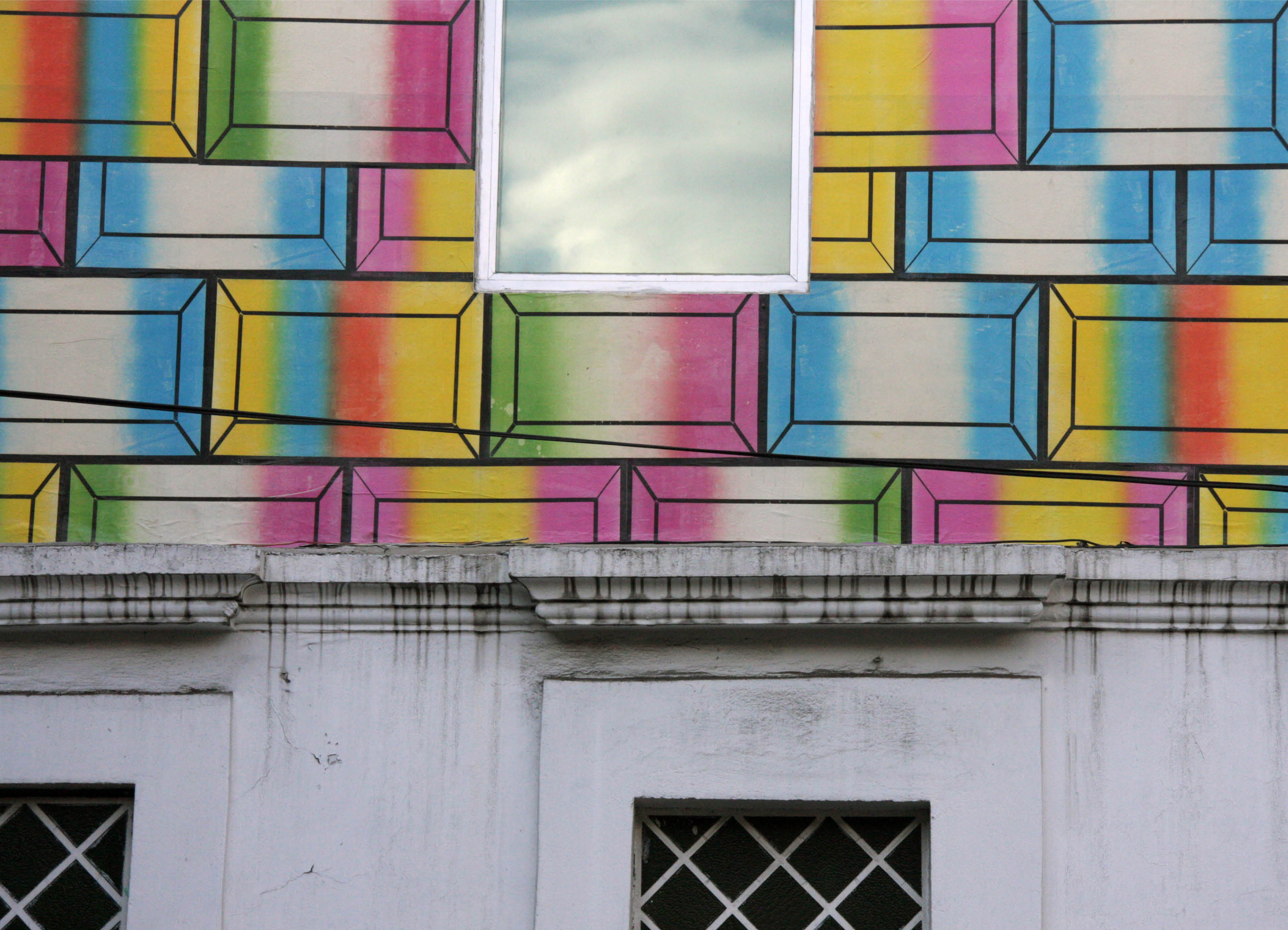 'Telon' detail of public art poster installation of Banderas posters by UK artist Henry Coleman with a view of architectural details and windows poking through brightly colored geometrical poster applied to the side of a building