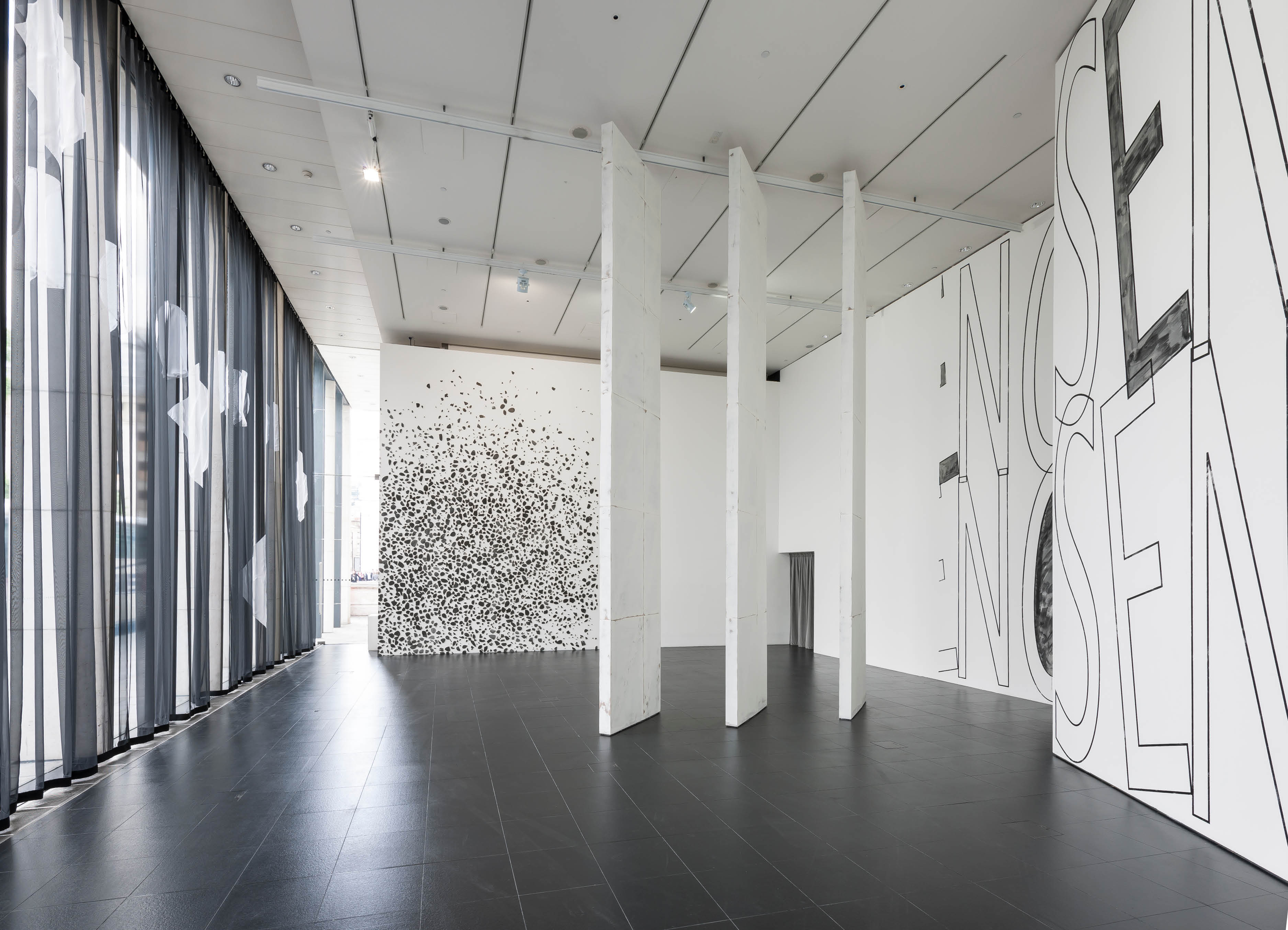 'About now' exhibition by Henry Coleman at Bloomberg SPACE, large scale sculptural  works fill the walls in black and white a voile curtain covers the windows and three large slanted panels divide the space 