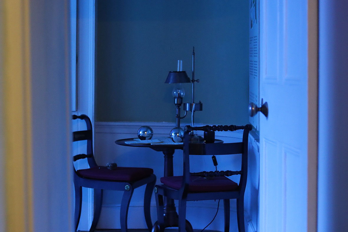 The effects', Sculptural installation by artist Henry Coleman. Drawing room of JMW Turner's House, Sandycombe Lodge bathed in blue colored light viewed through a doorway, two reflective globes and a lamp  sit on an ornate table