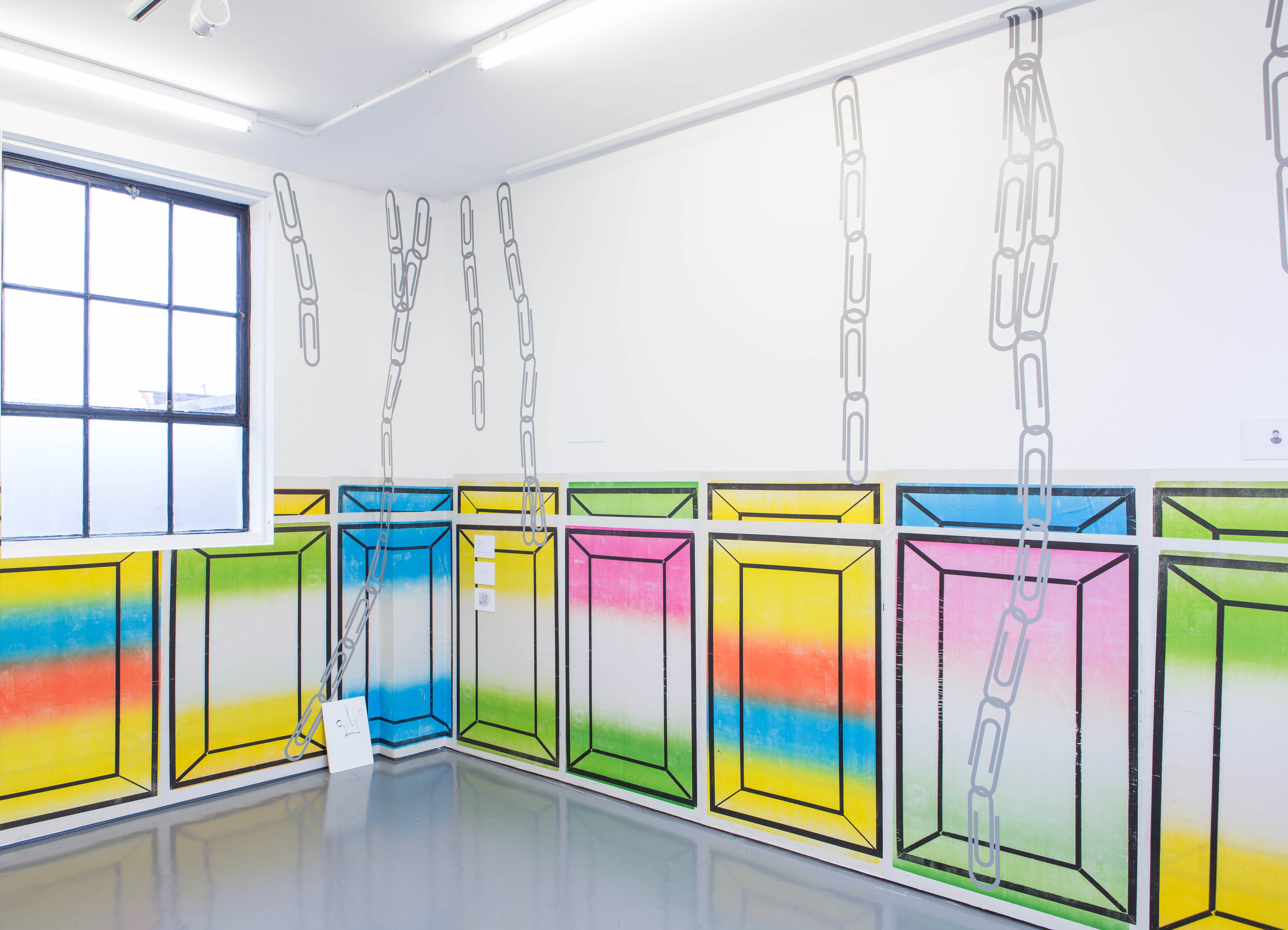 Installation view of 'Half' by henry Coleman, brightly colored posters overlap to horizontally  fill  half the available wall space of a small gallery space with vinyl paperclip artwork by Paul Schneider running over the top