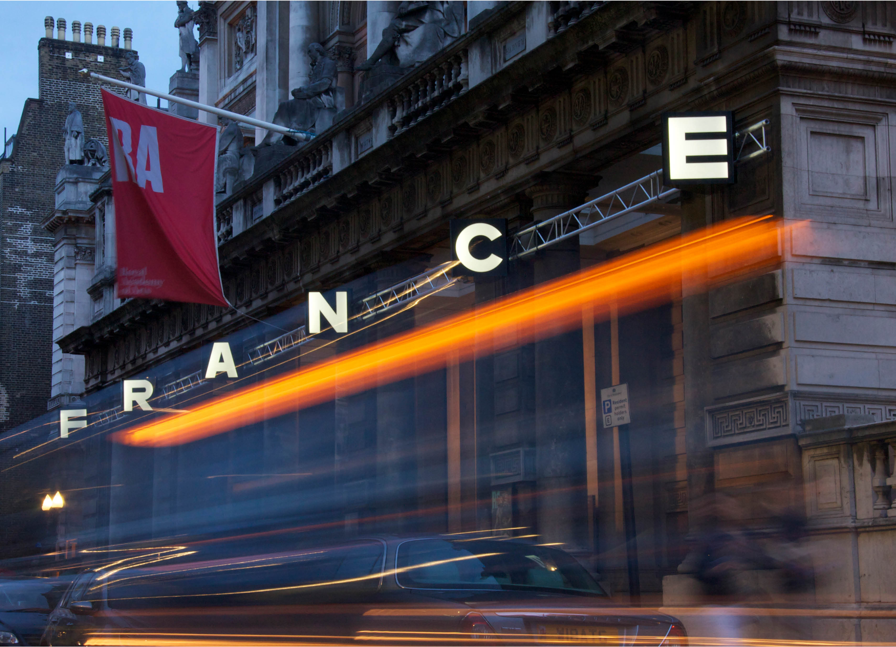 'Scrape' by Uk Artist Henry Coleman. Sculptural installation of illuminated signage spelling out the word FRANCE attched to the facade of the RA building 6 Burlington Gardens, London at dusk with a passing taxi light