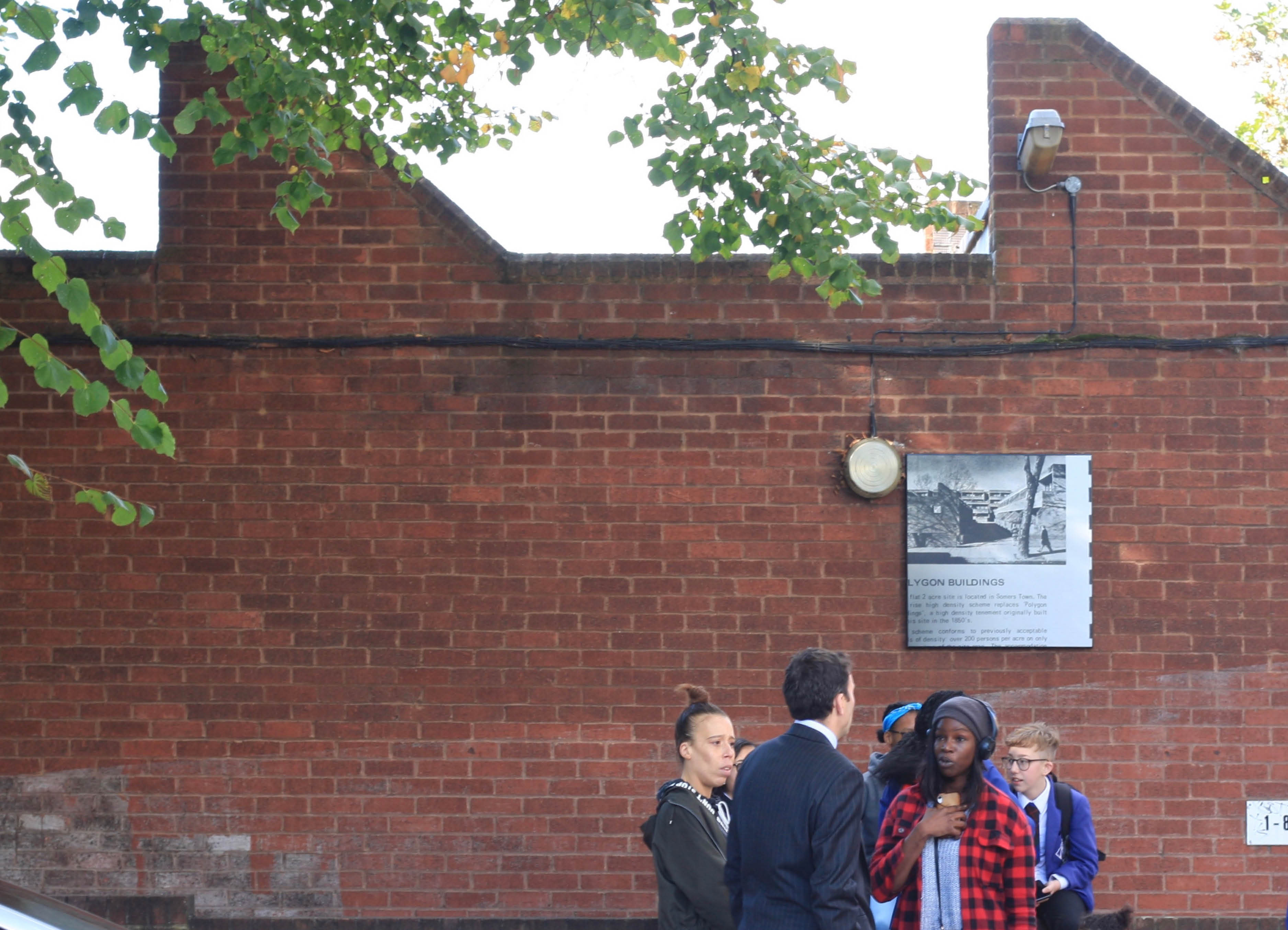 Polygon Buildings' by architectural intervention by Henry Coleman, A black and white sign image replaces the estate map for Polygon estate in Somers Town by Architect Tabori, a group of people talk in the foreground