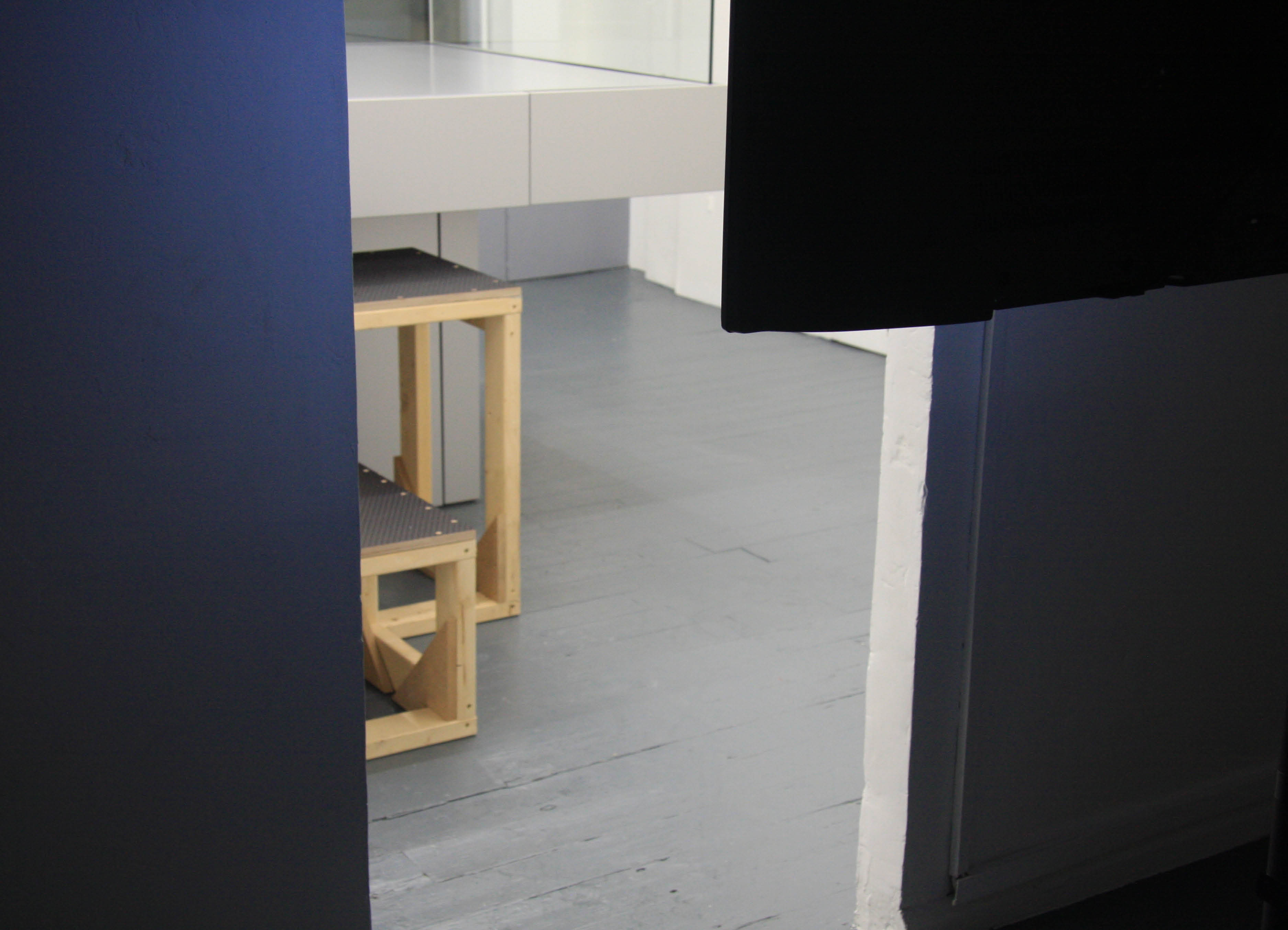 'My Sky' exhibition  by artist Henry Coleman at Chalton Street gallery, a view through a doorway of bleacher staging and raised balcony sculpture from inside a a dark film viewing room