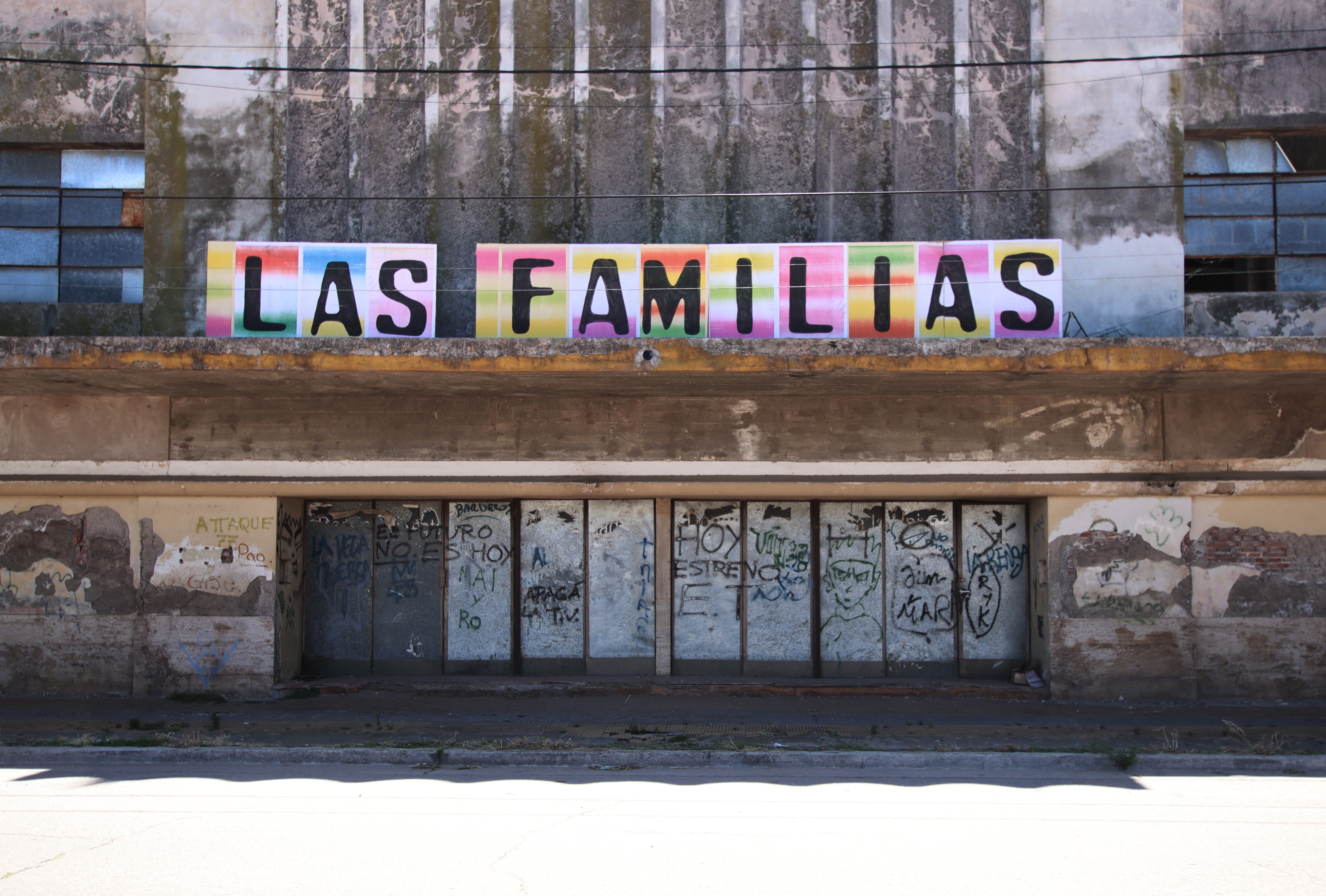 Las Familias (2025) by Henry Coleman: Poster Sculpture installtion in black serif letters on Argentine Litho Pare above weathered, graffitied entrance doors of Cinema Grand Sud. 
