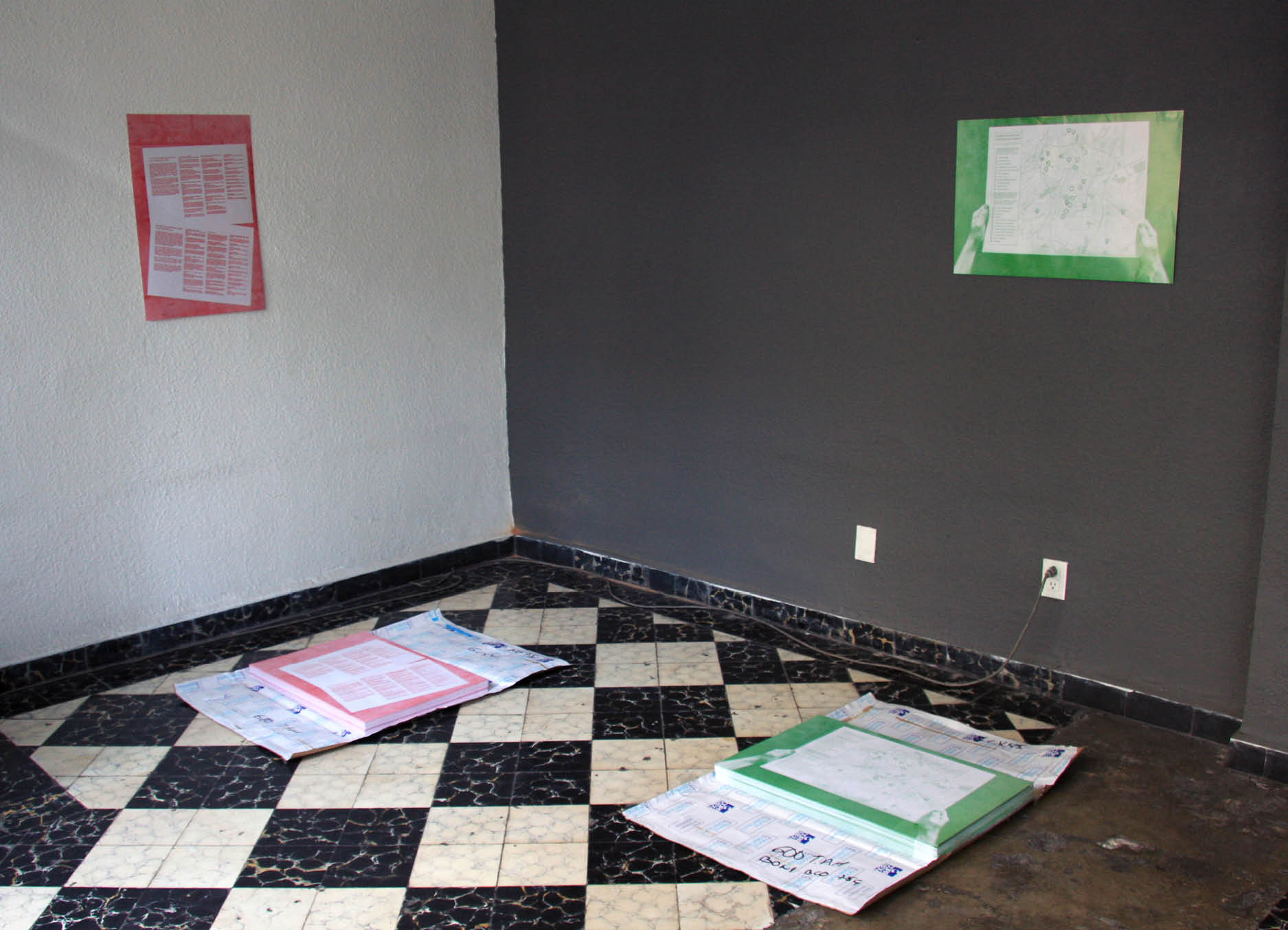 'Una Mapa Una Lista' by Henry Coleman produced for SOMA, Mexico City,  Two stacks of artwork posters on the work of the Architect Juan O'Gorman  in red white and green lie in front of two artworks presented on the wall in the exhibition 'you can't choose your neighbors' SOMA Mexico 