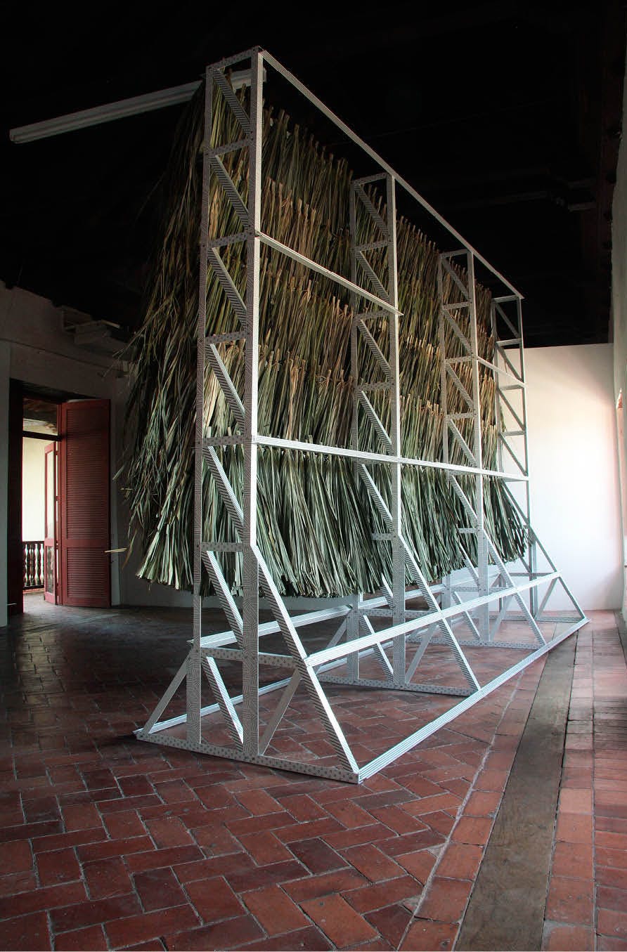 Decorated structure (productive public) by artist Henry Coleman, produced for Salon nacional de Artistas, Cartagena, Colombia, Rear view of large wall of palapa thatch mounted onto decorated white advertising hoarding frame on a simple tiled floor