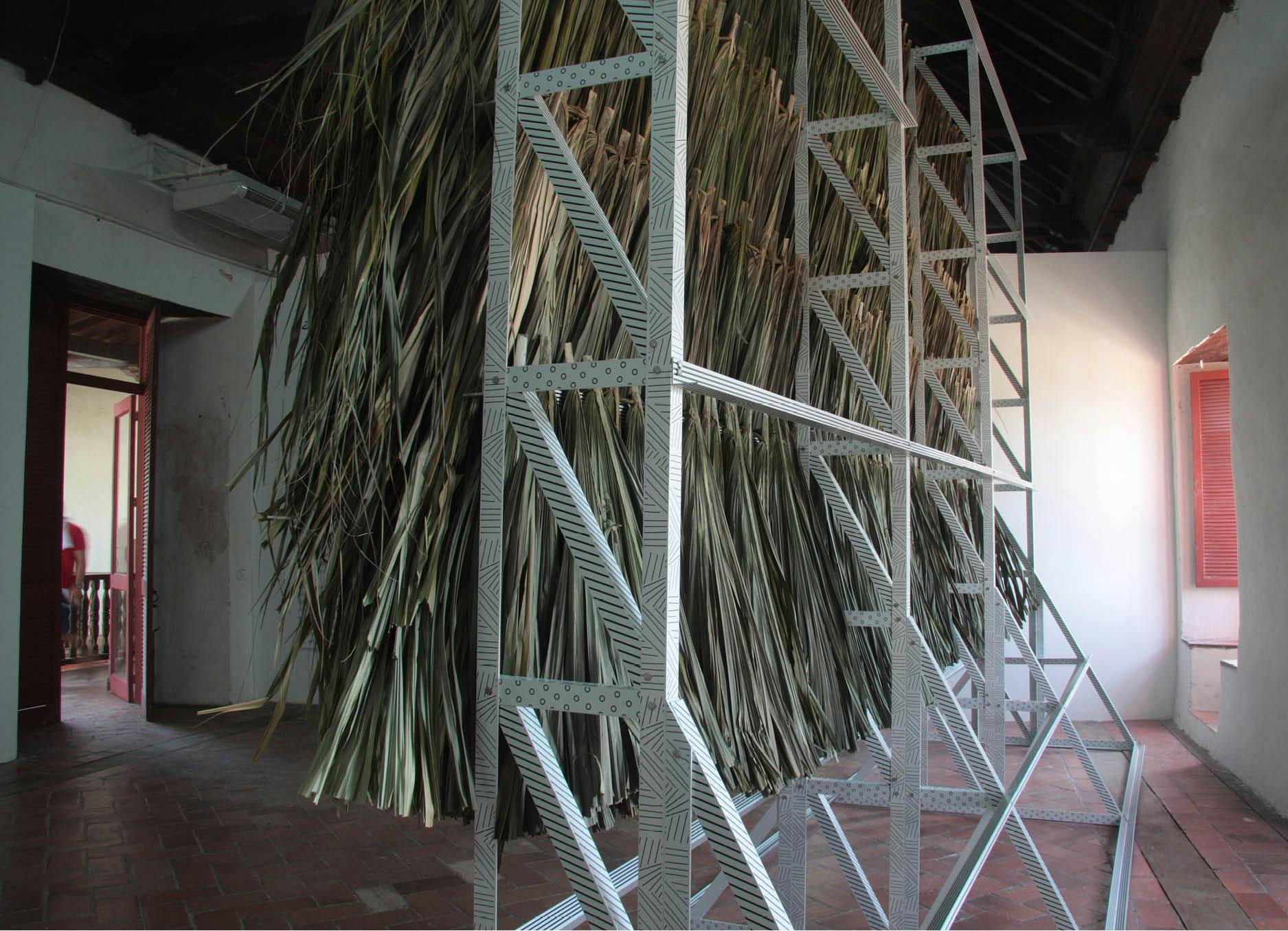 Decorated structure (productive public) by artist Henry Coleman, produced for Salon nacional de Artistas, Cartagena, Colombia, Close up Rear view of large wall of palapa thatch mounted onto white frame with intricate vinyl decoration frame on a simple tiled floor