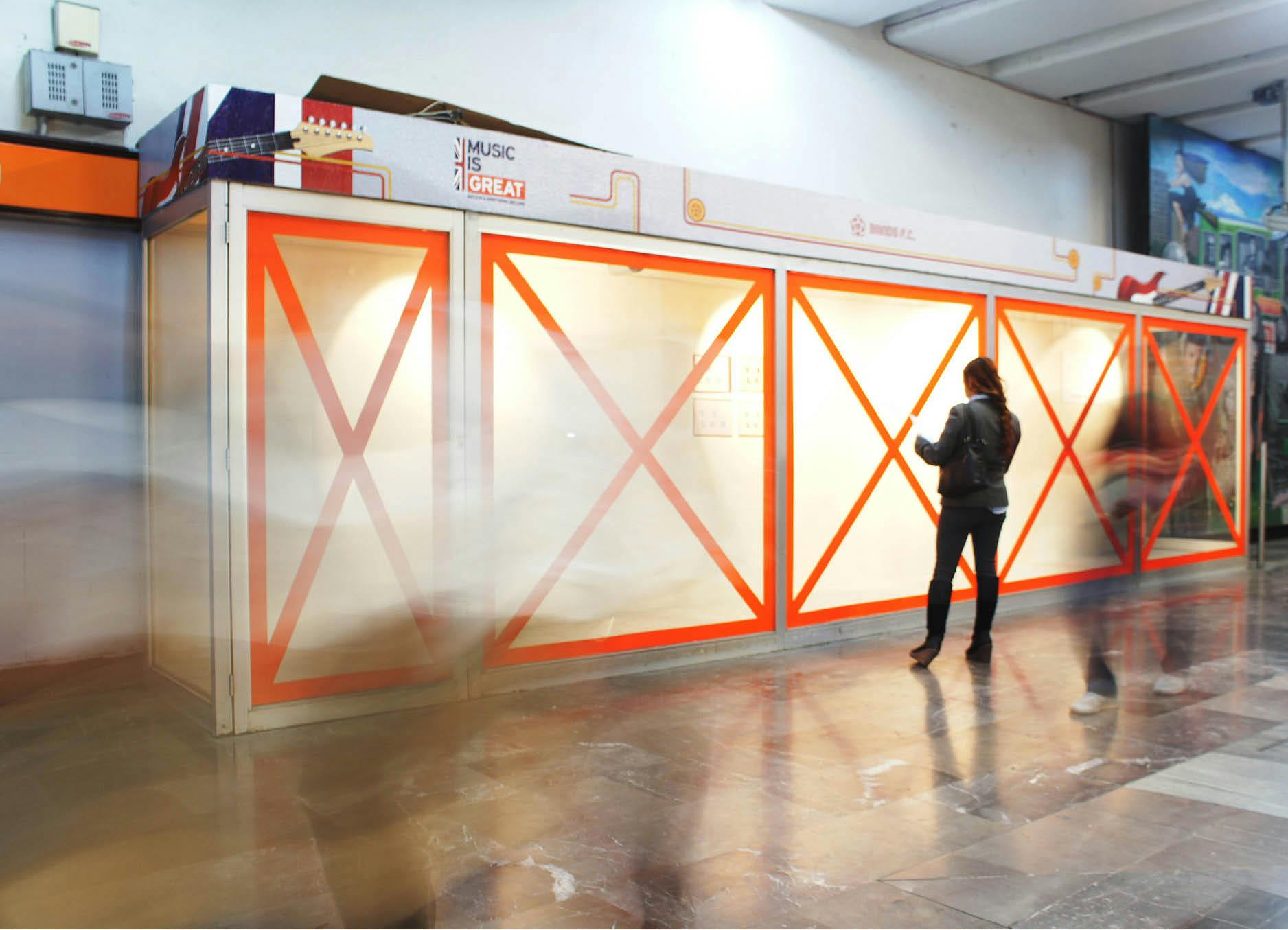 Public artwork 'Telon' by Artist Henry Coleman installed at Mexico city Metro Station Auditorio with vibrant orange vinyl crosses applied to a large vitrine with a woman looking inside whilst blurred figures move past