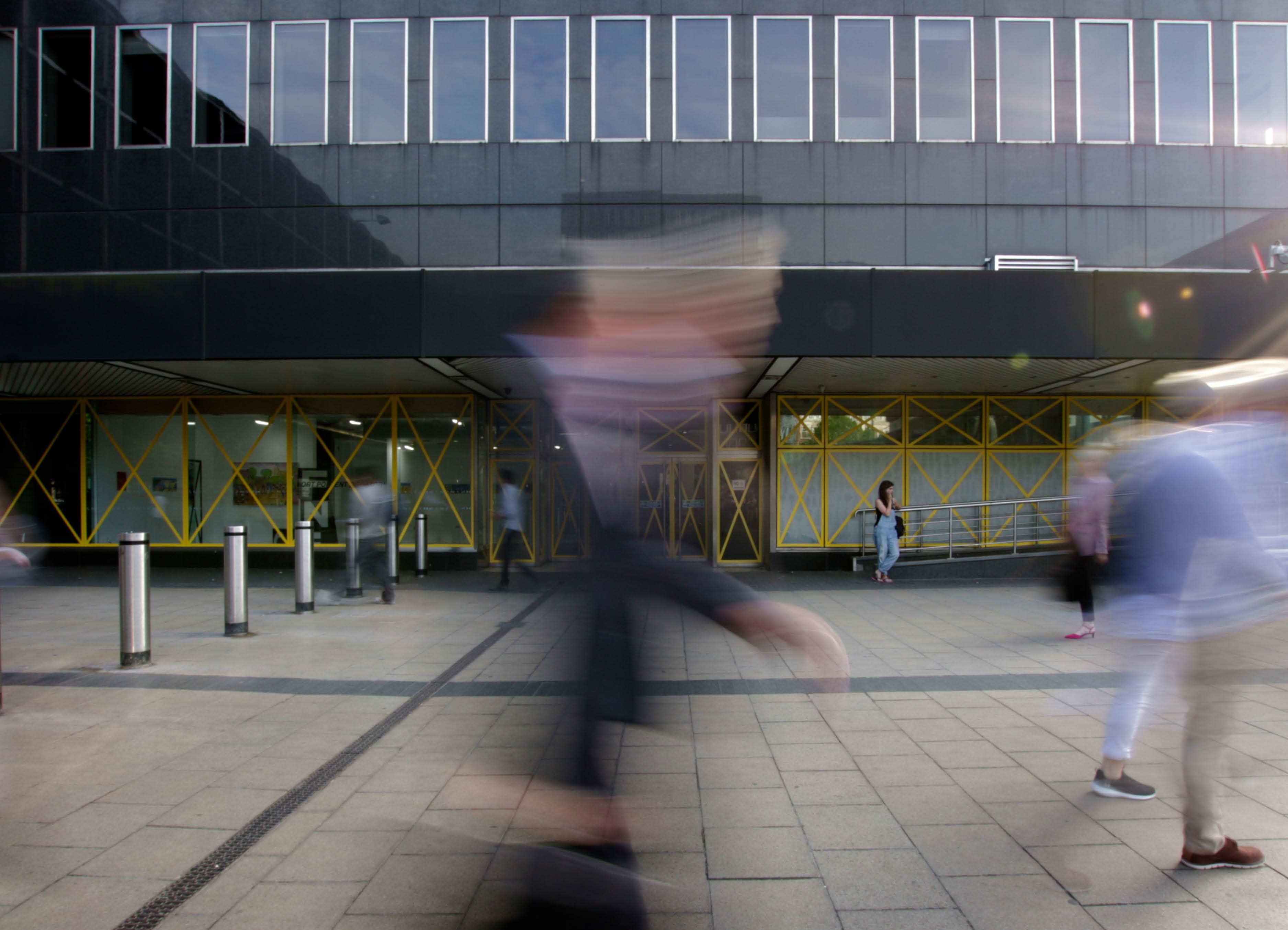 Port Portal Piscator' Vinyl installation by artist Henry Coleman of yellow vinyl crosses across the modernist façade of old Euston station forecourt building by Seifert and Partners, now destroyed, with blurred figures walking in the foreground