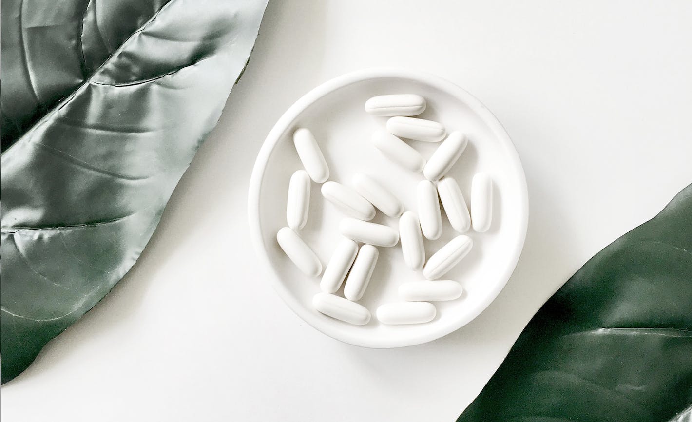 Several pills placed in a small white cup, with leaves framing the image. 