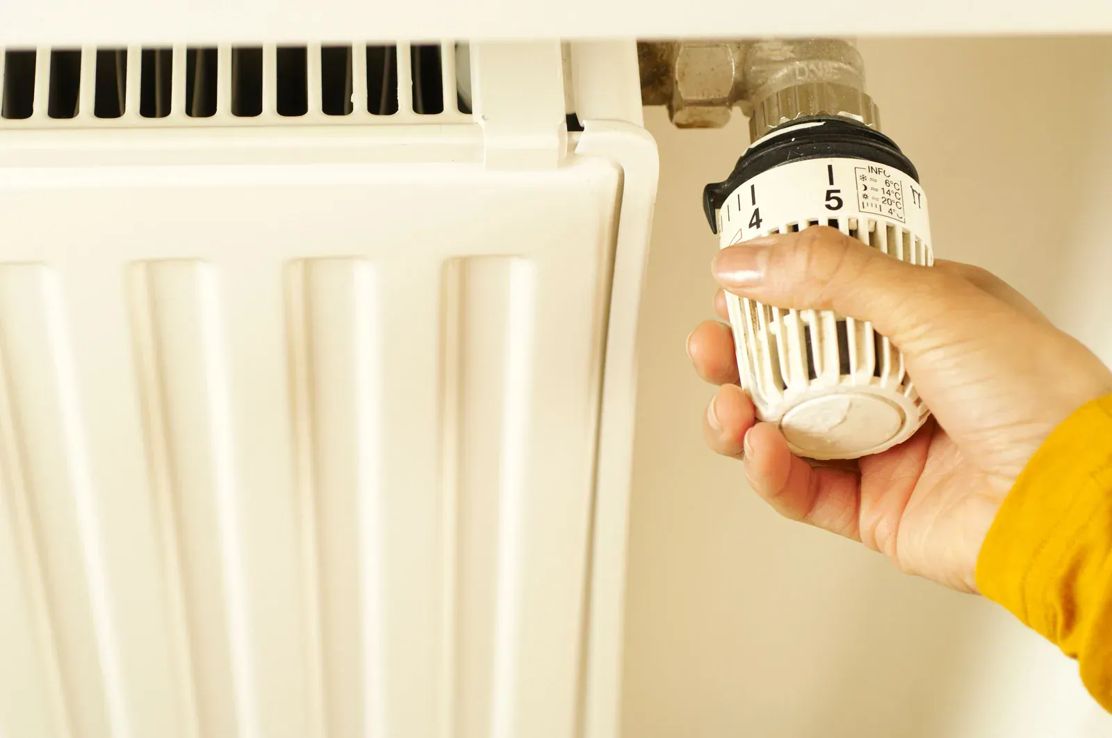 Main réglant le robinet thermostatique d'un radiateur blanc dans un logement