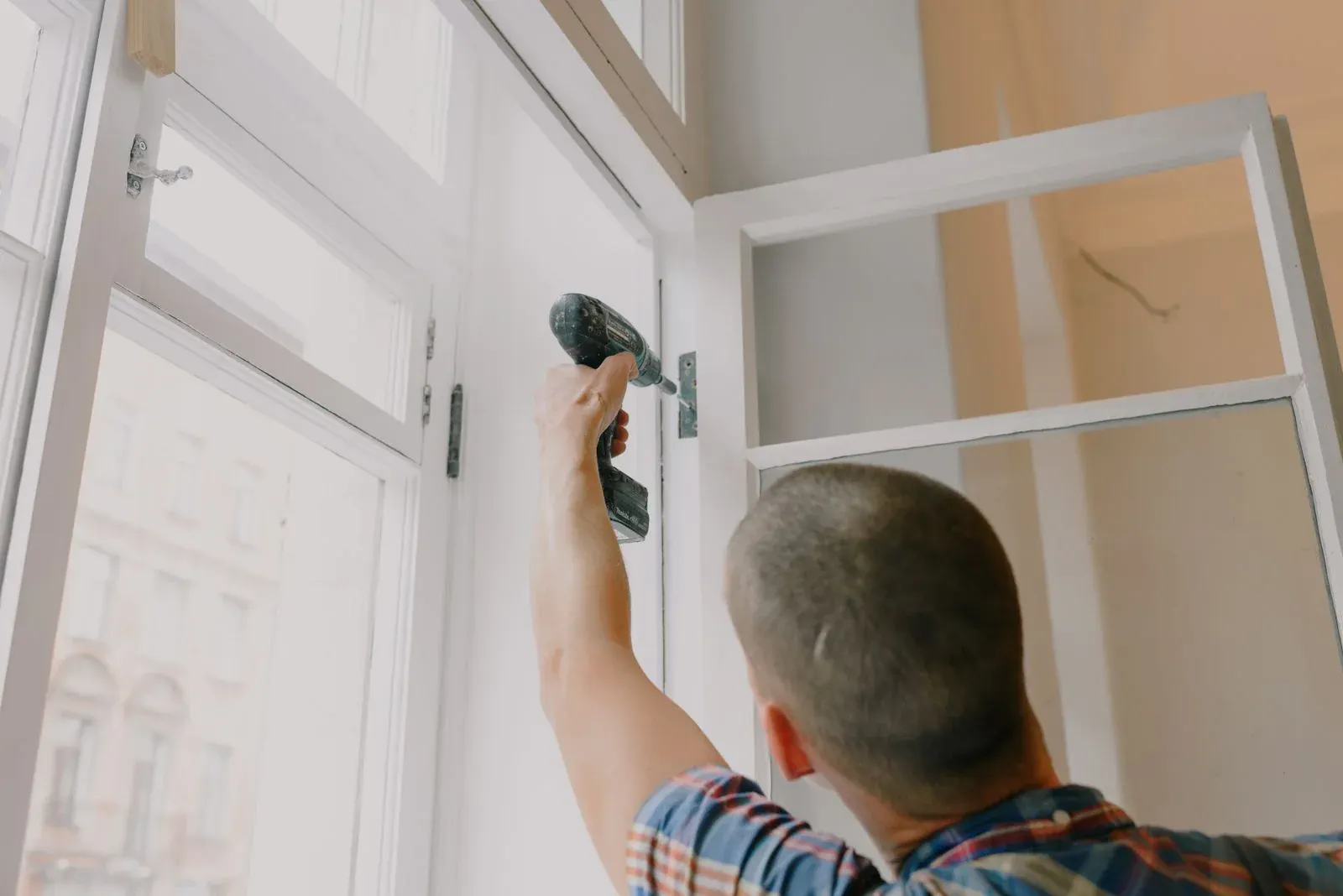 Artisan vu de dos fixant une fenêtre à la visseuse dans un appartement ancien en rénovation