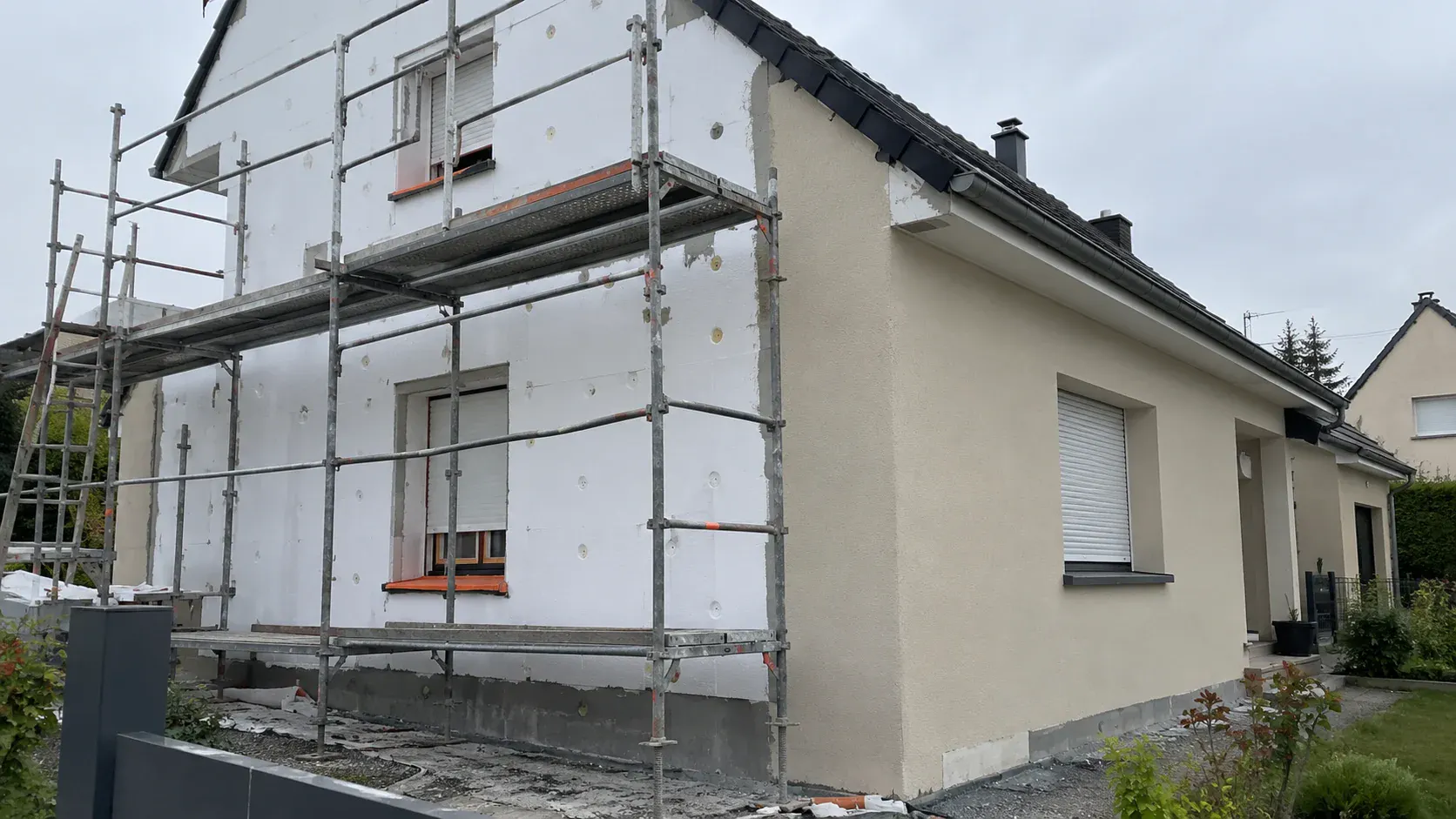 Façade en cours d'isolation par l'extérieur : panneaux isolants posés sous échafaudage, enduit de finition sur une partie