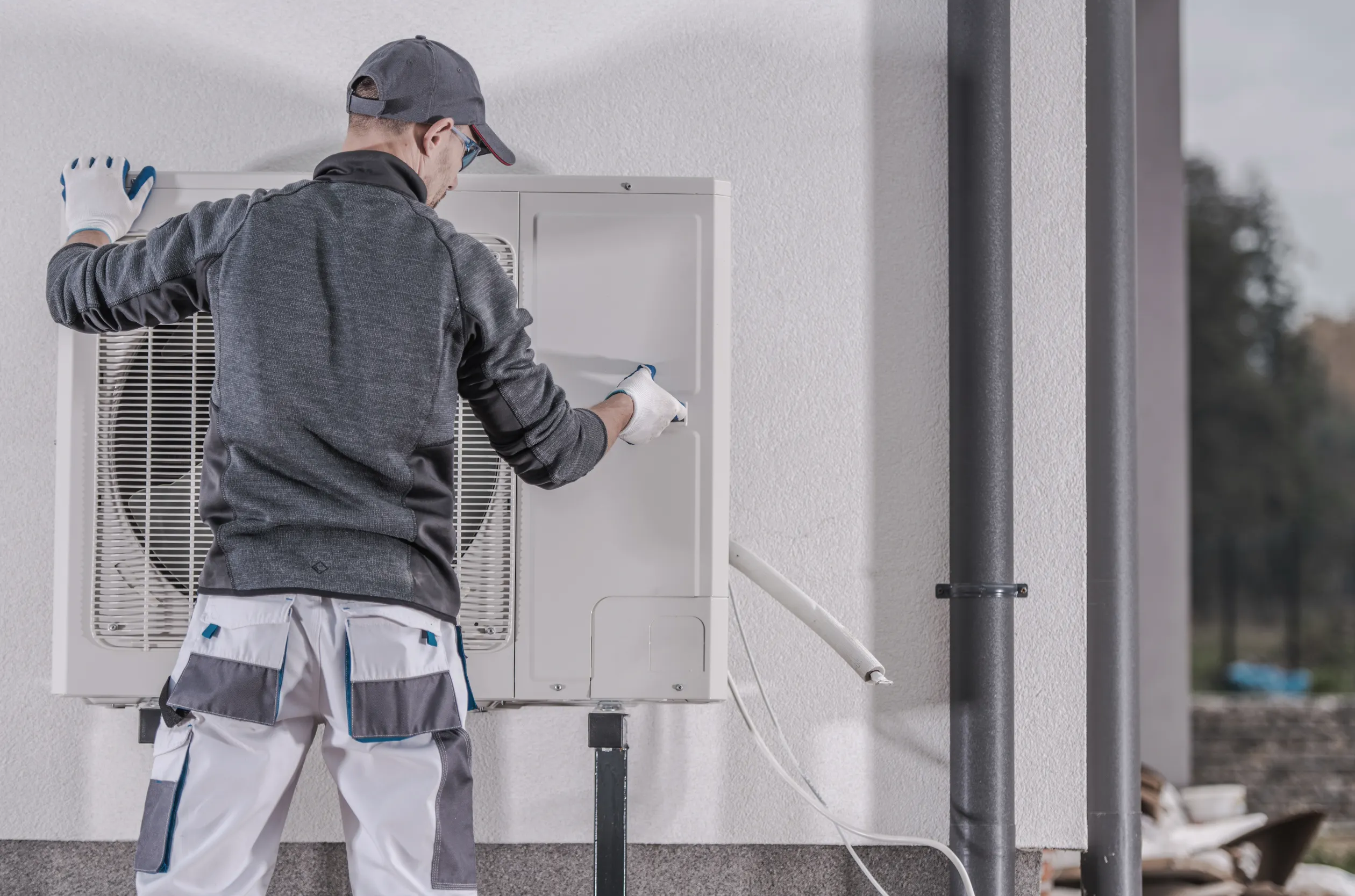 Technicien intervenant sur une unité extérieure de pompe à chaleur fixée au mur