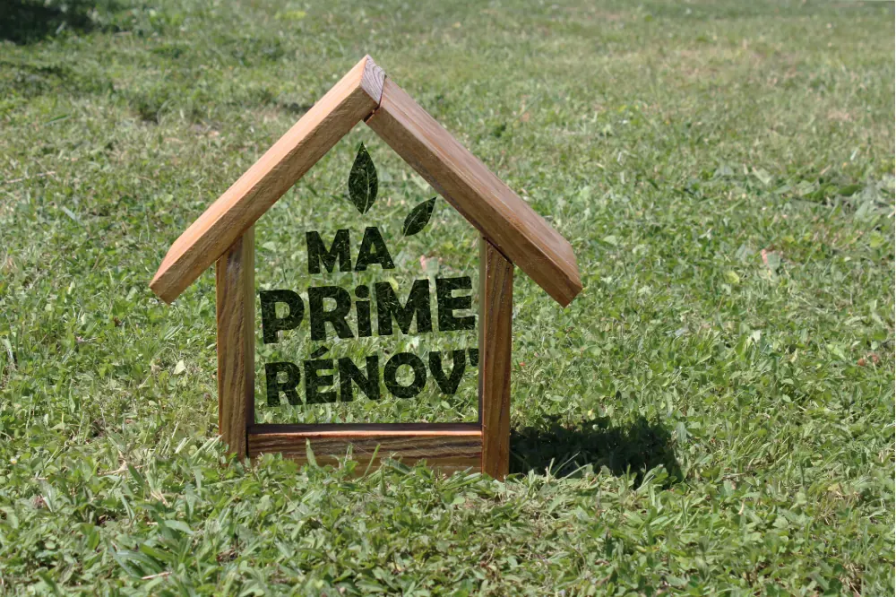 Cadre en bois en forme de maison marqué « Ma Prime Rénov' » sur l'herbe