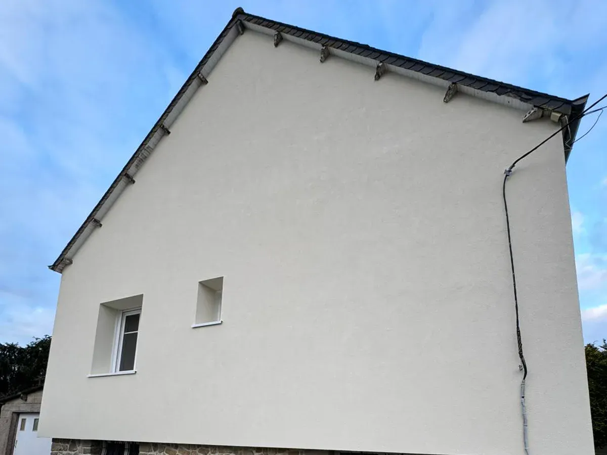 Maison isolée par l’extérieur dans le cadre d’une rénovation d’ampleur, Bretagne : pignon entier en enduit clair, au-dessus d’un soubassement en pierre