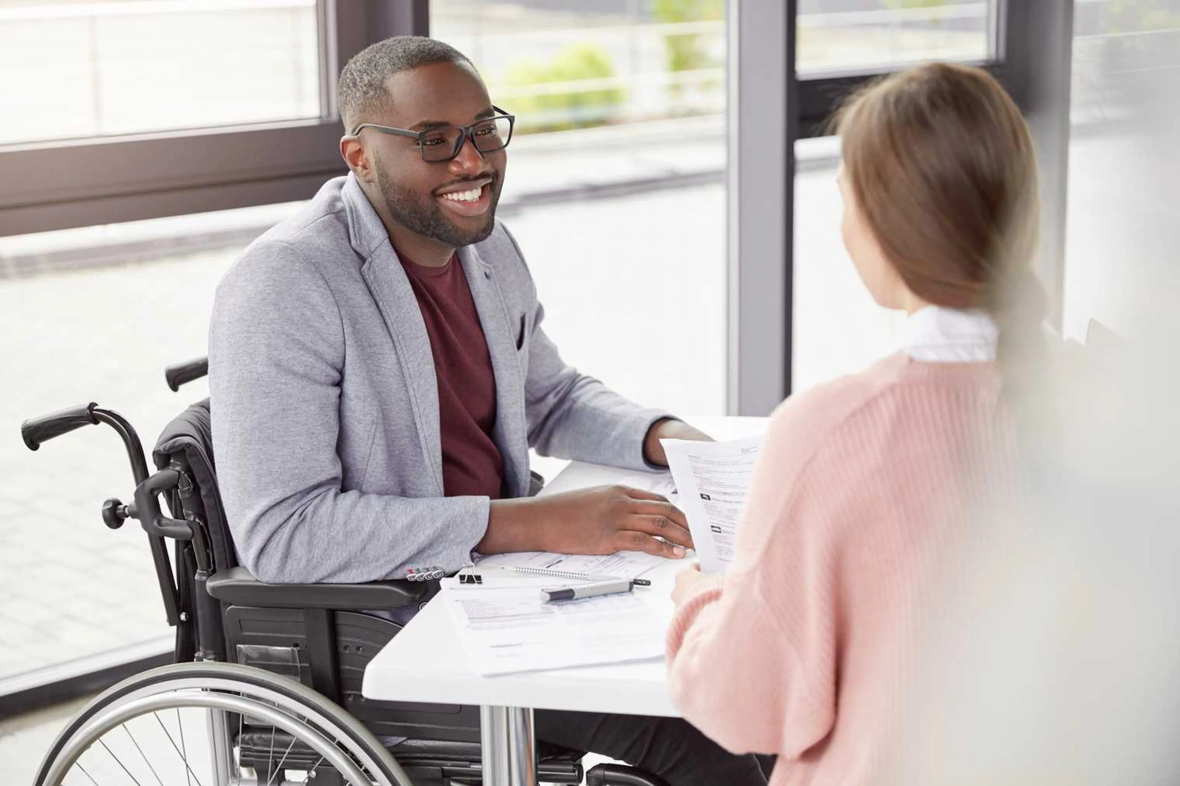 Young man in a wheelchair sits at a table with a woman holding papers